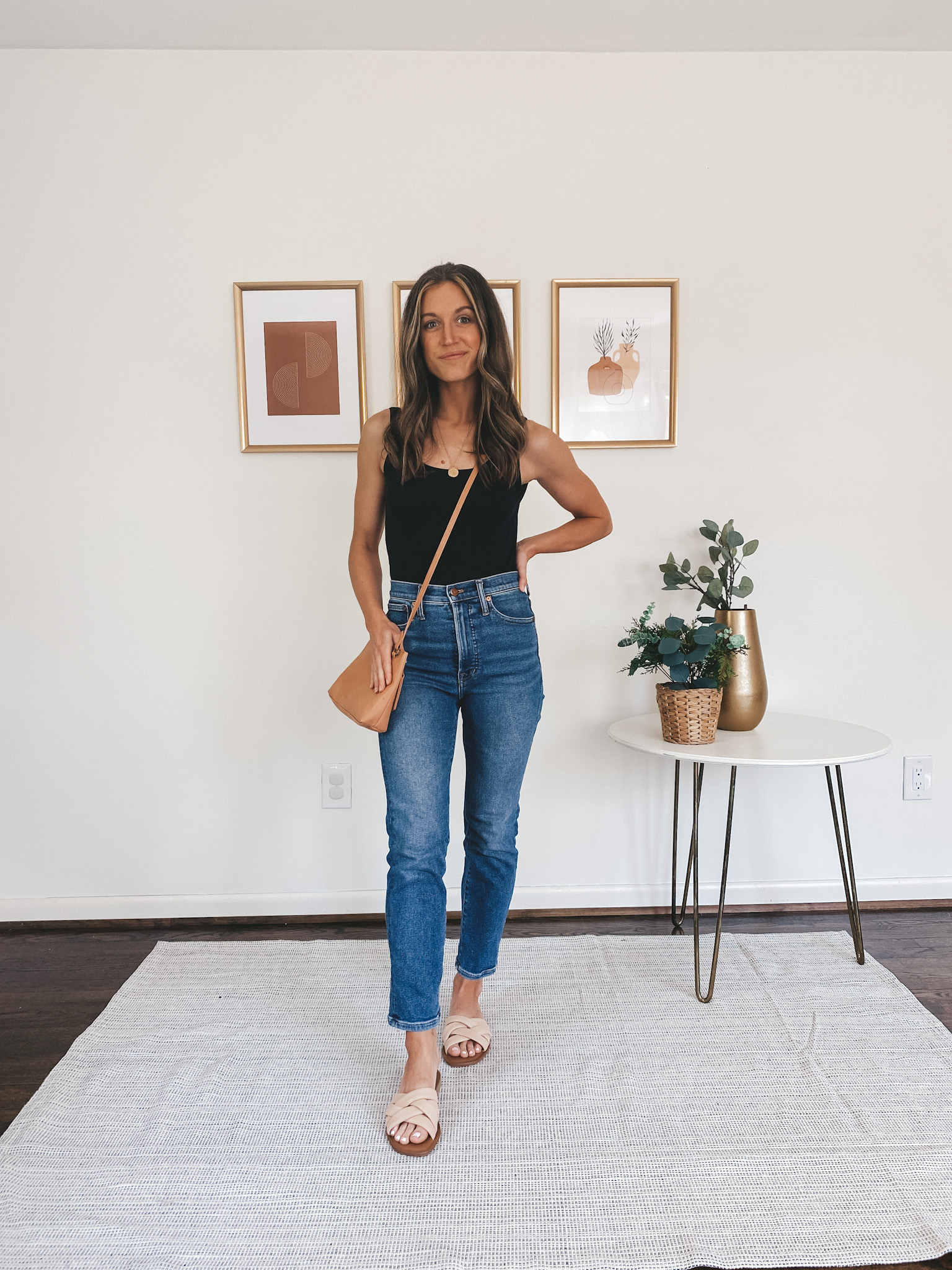 ashley wearing a black bodysuit, mid-wash straight leg denim, nude padded slides and a camel colored crossbody bag