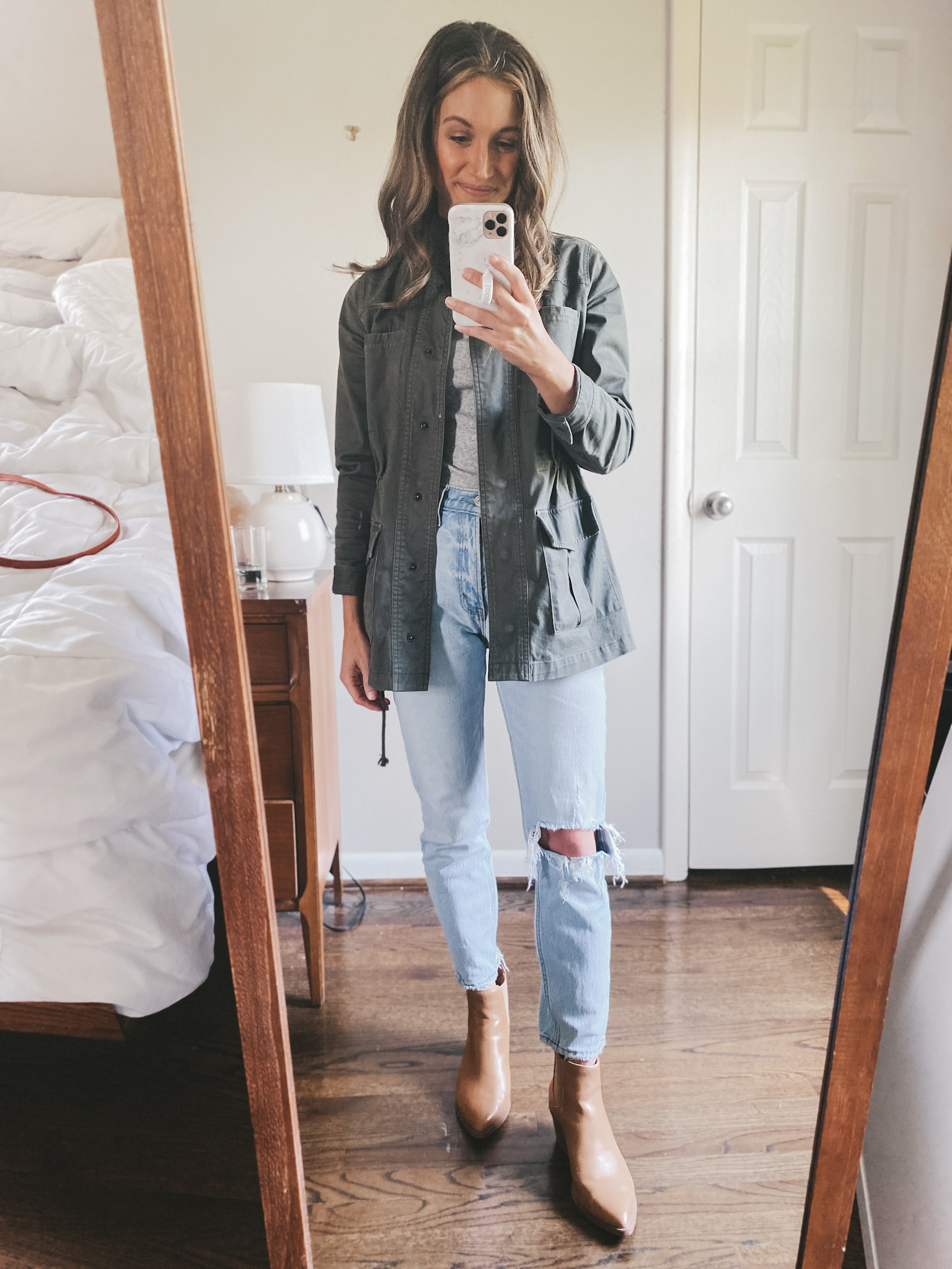 ashley wearing a gray tee, green utility jacket, distressed mom jeans, and camel colored ankle boots