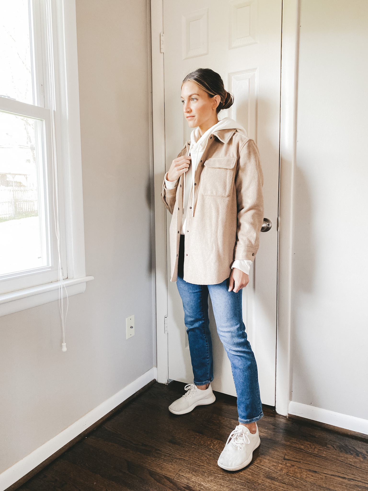 ashley wearing a cream hoodie, tan shacket, mid-wash straight leg denim and wool runners