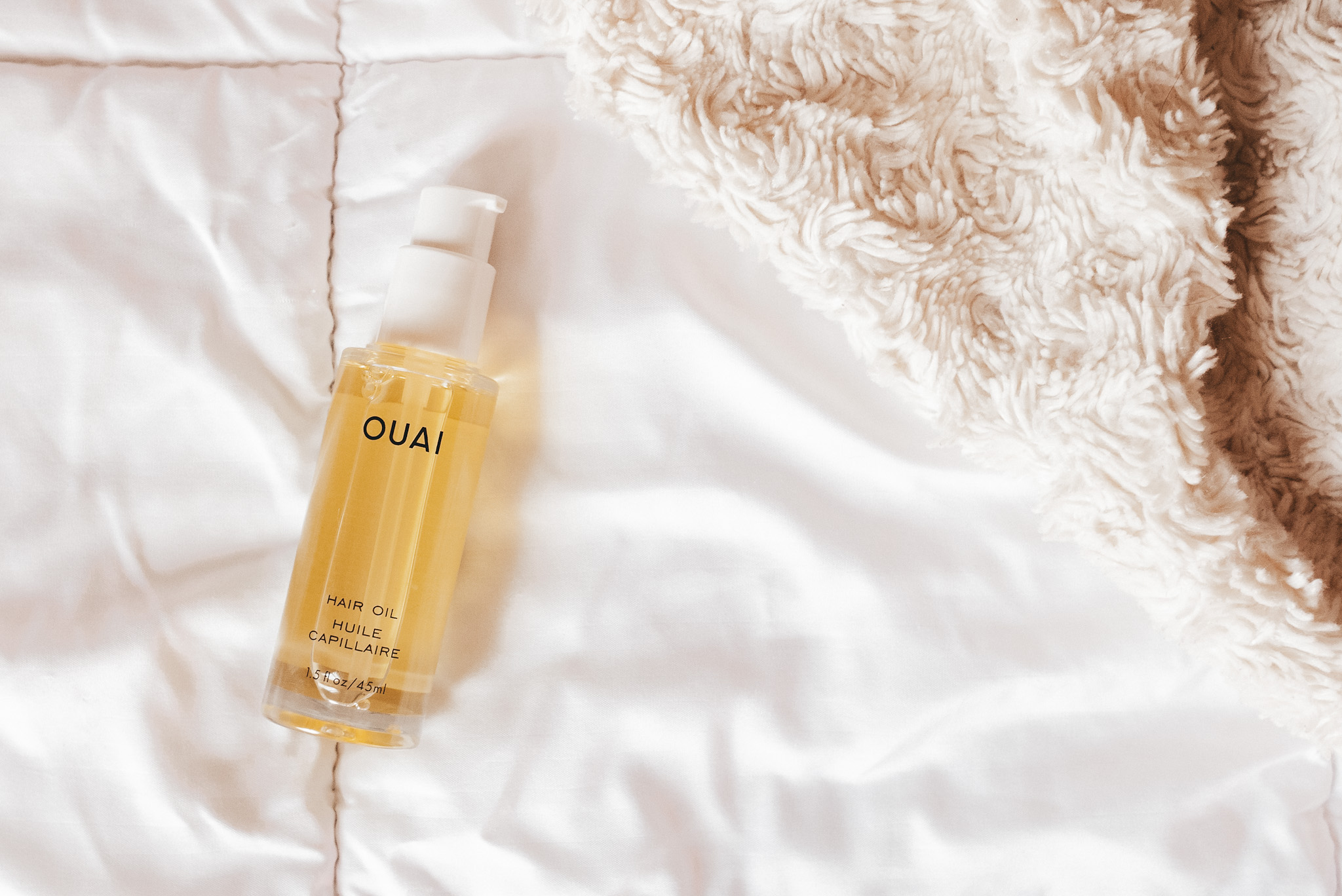 a bottle of Quai Hair Oil on a white comforter