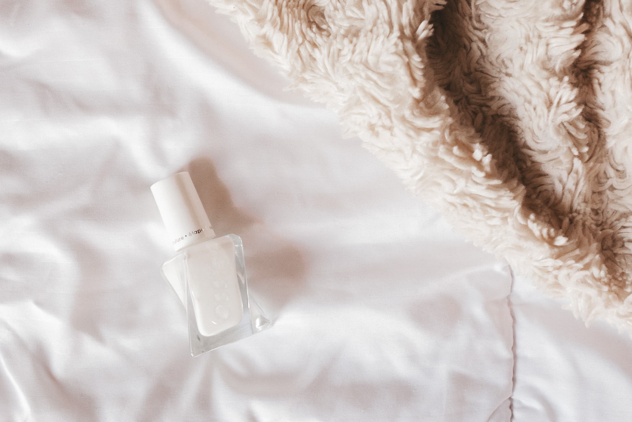 a white comforter with a bottle of Essie Gel Couture white nail polish