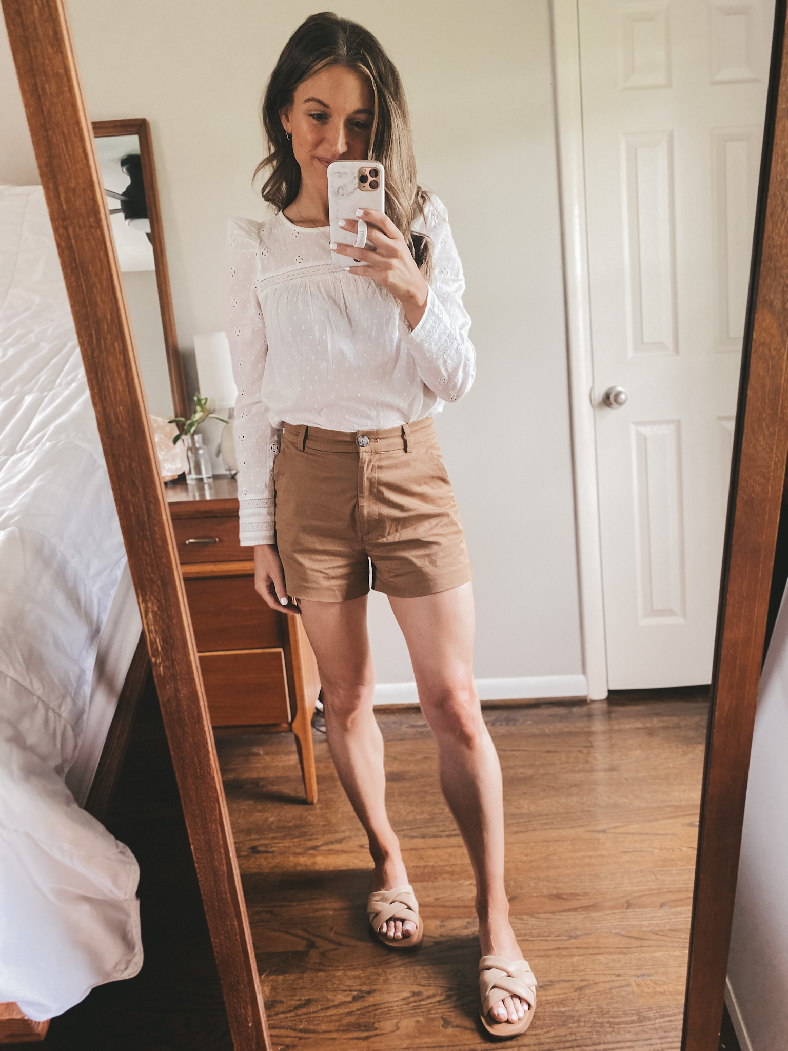a mirror selfie with ashley wearing an eyelet top and cognac twill shorts with nude padded slides