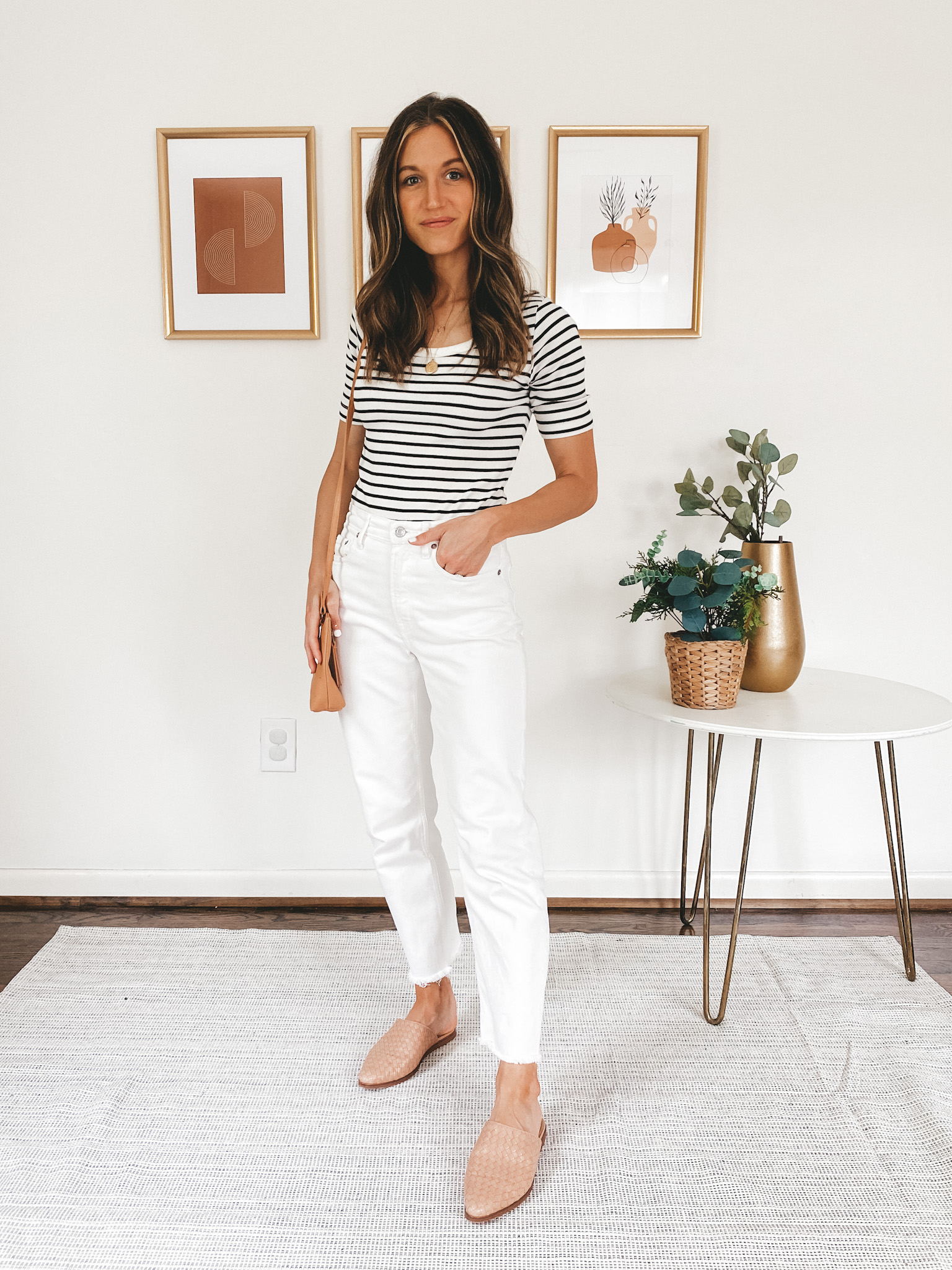 ashley wearing a striped tee, white straight leg denim, tan woven mules and a camel colored crossbody bag
