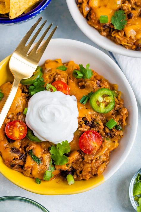 a yellow and white bowl with spaghetti squash taco bake topped with sour cream