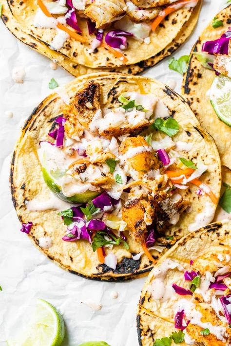 four cod fish tacos topped with cabbage, lime yogurt sauce and cilantro