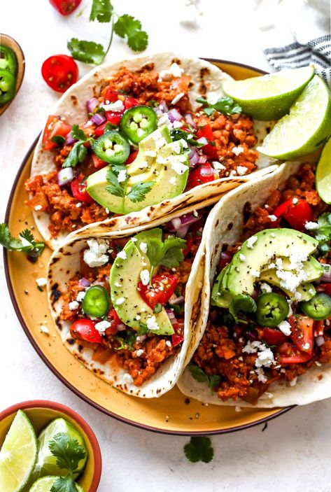 a plate with 3 turkey tacos topped with avocado and tomatoes, sliced limes on the side