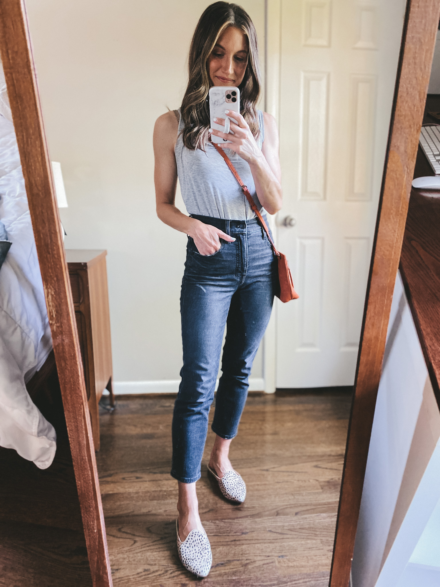 a mirror selfie of ashley wearing a gray tank, black straight leg denim, leopard mules and a red crossbody bag