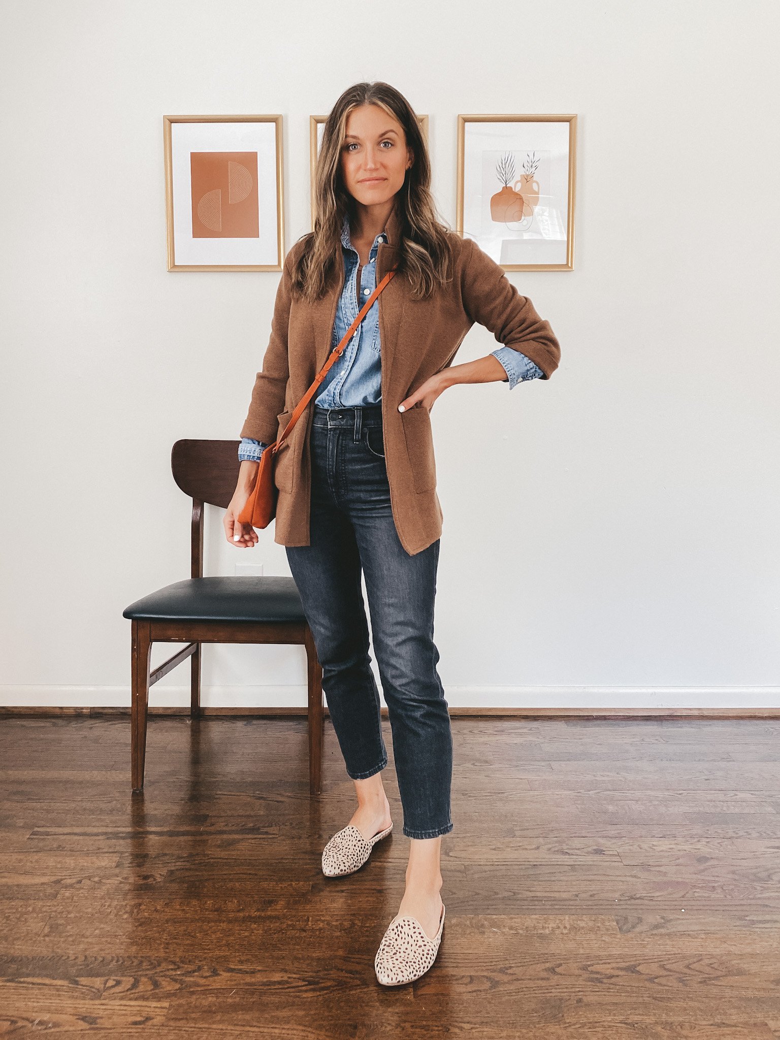 ashley wearing a chambray button down top, brown sweater blazer, wash black denim, nude padded slides and a red crossbody bag