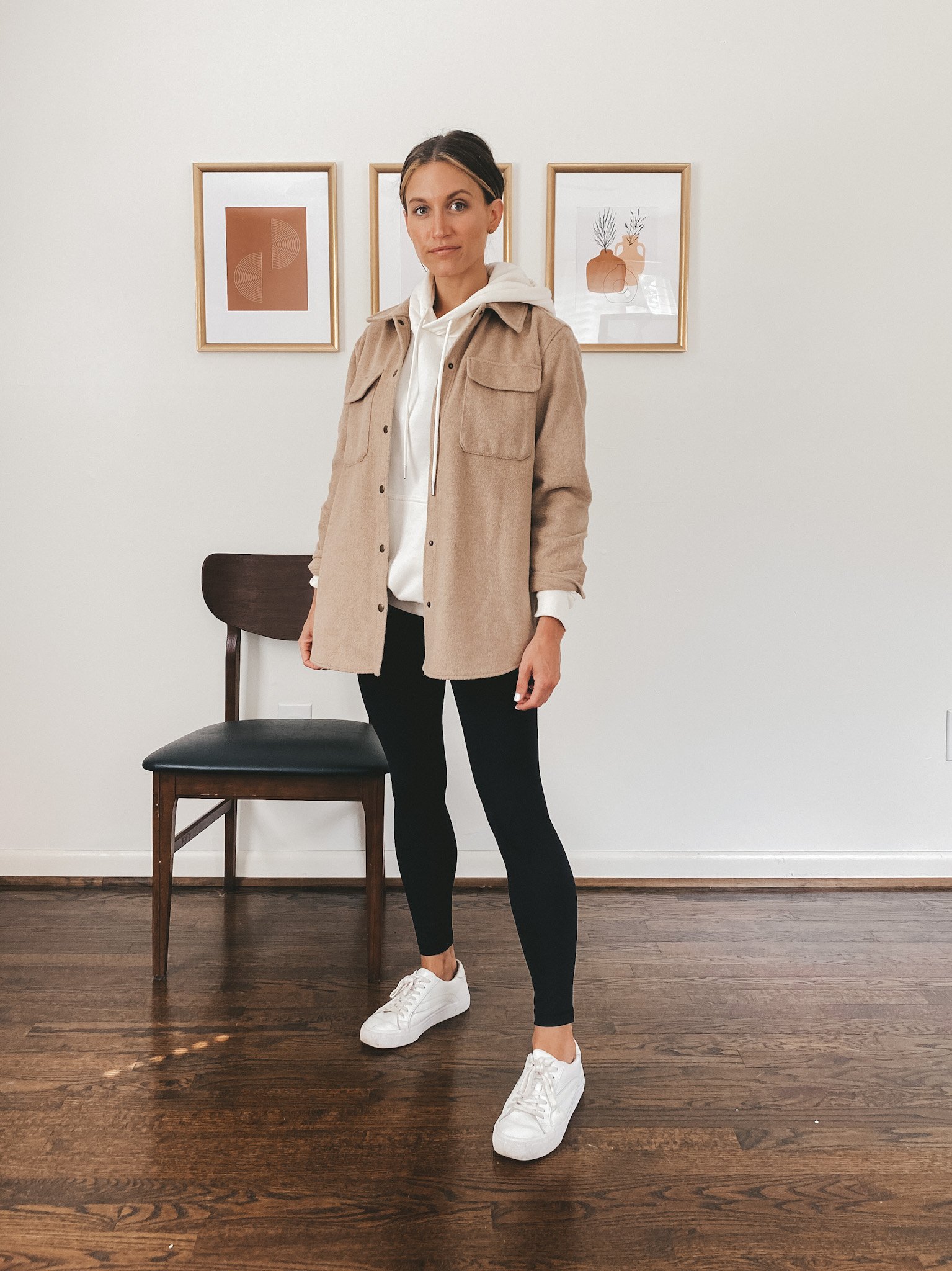 ashley wearing a cream colored hoodie, tan shacket, black leggings and white sneakers