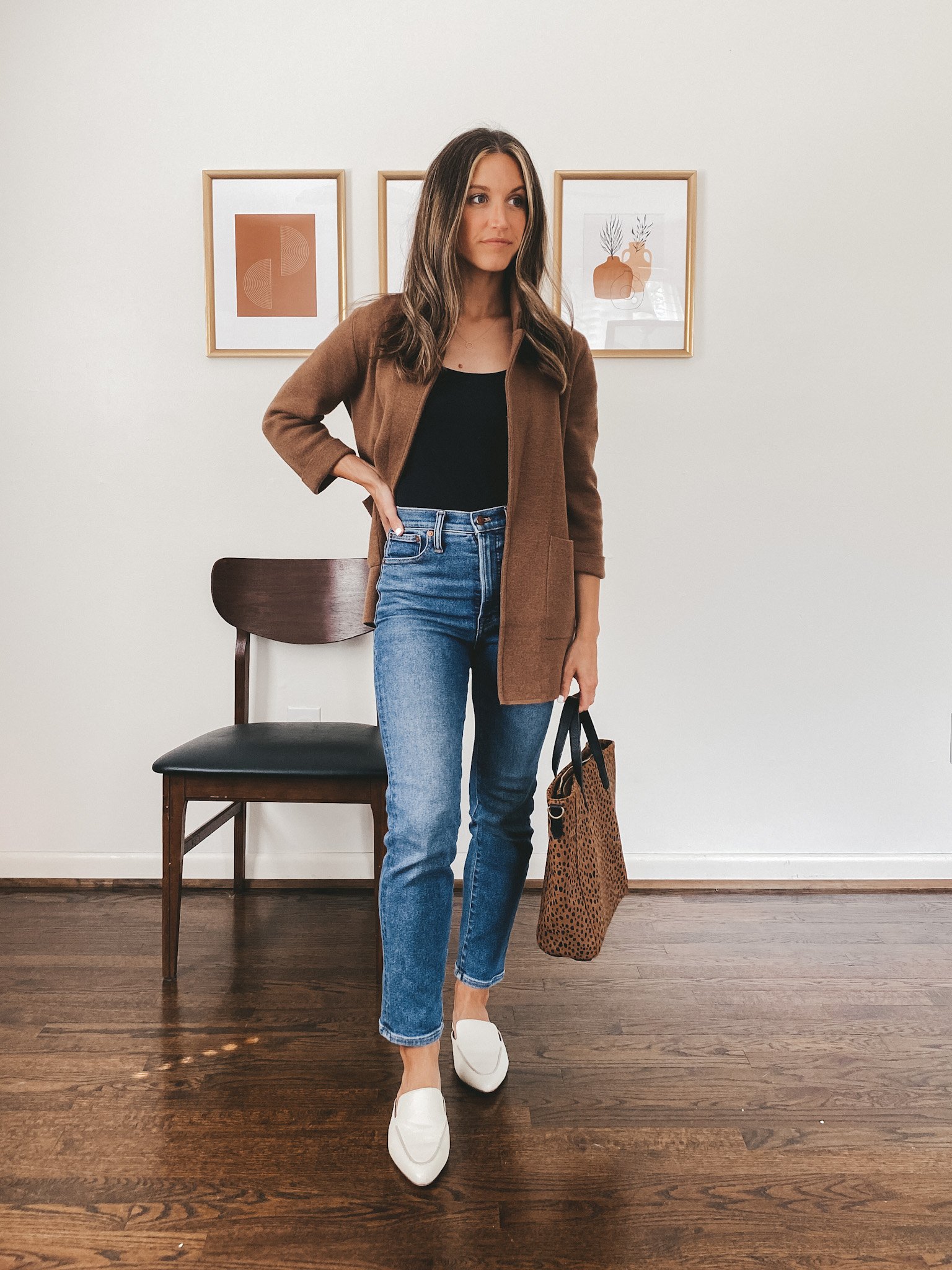 ashley wearing a sleeveless black bodysuit, brown sweater blazer, mid-wash denim and white mules carrying a leopard print tote bag