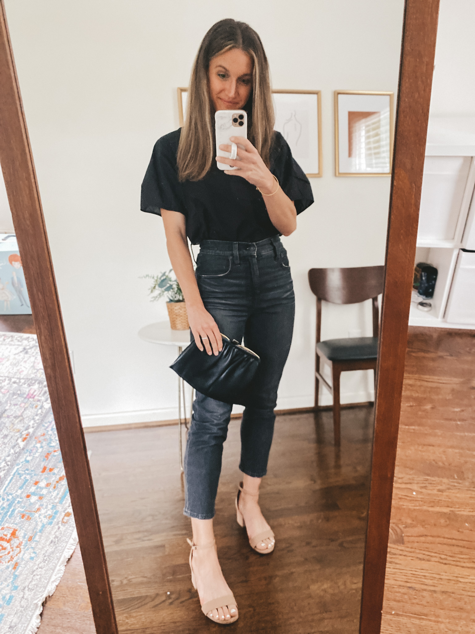 ashley wearing a black short sleeved top, washed black straight leg denim, nude block heel sandals, and carrying a vintage leather clutch