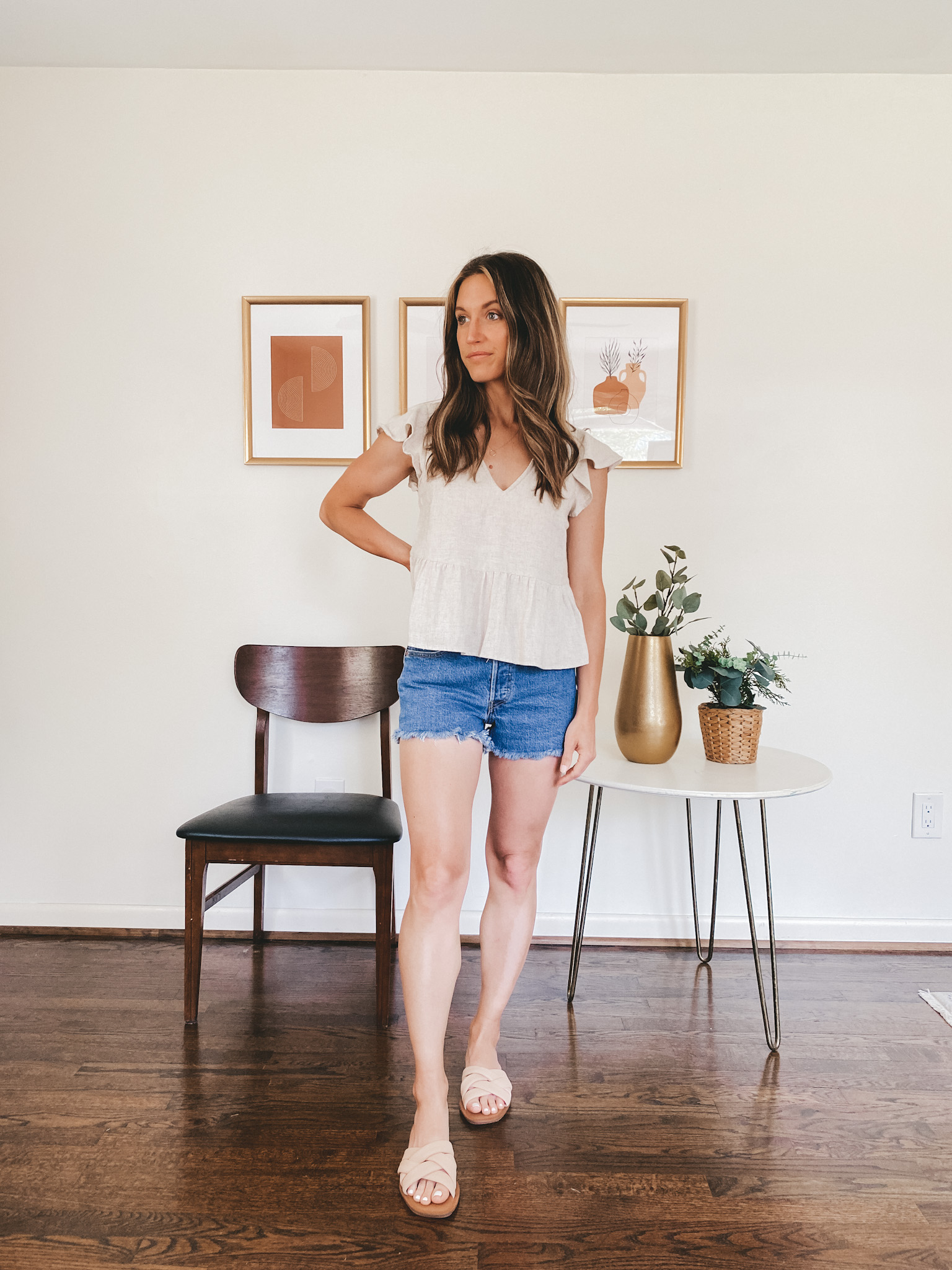 ashley wearing a tan linen blend flutter sleeve top, cut-off denim shorts, and nude padded slides