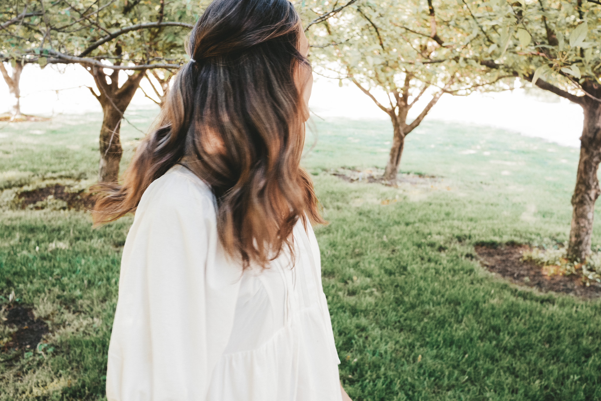 ashley standing between some trees wearing a white dress with her head turned backward
