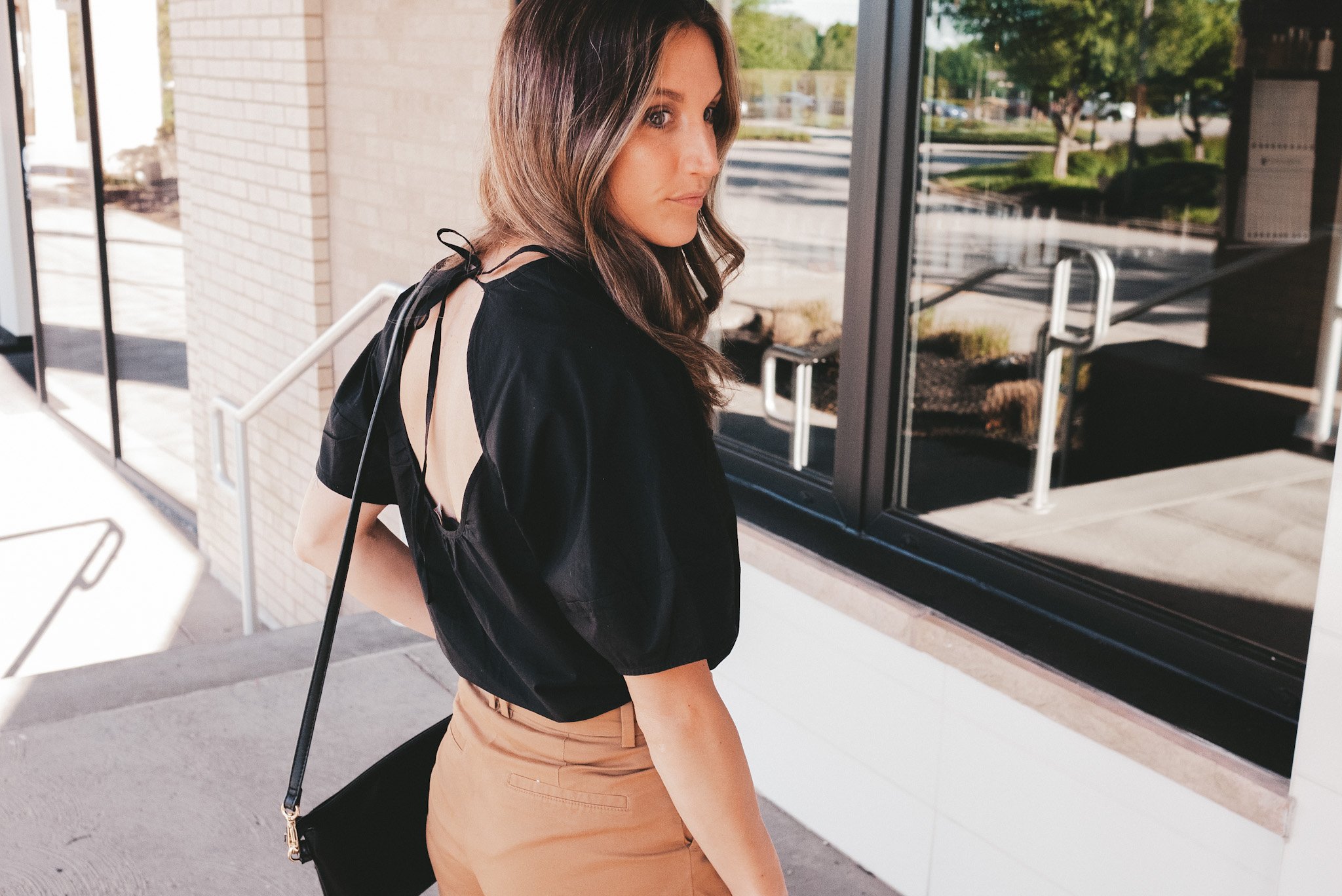 ashley wearing a circle back top, brown shorts standing in front of a shop window