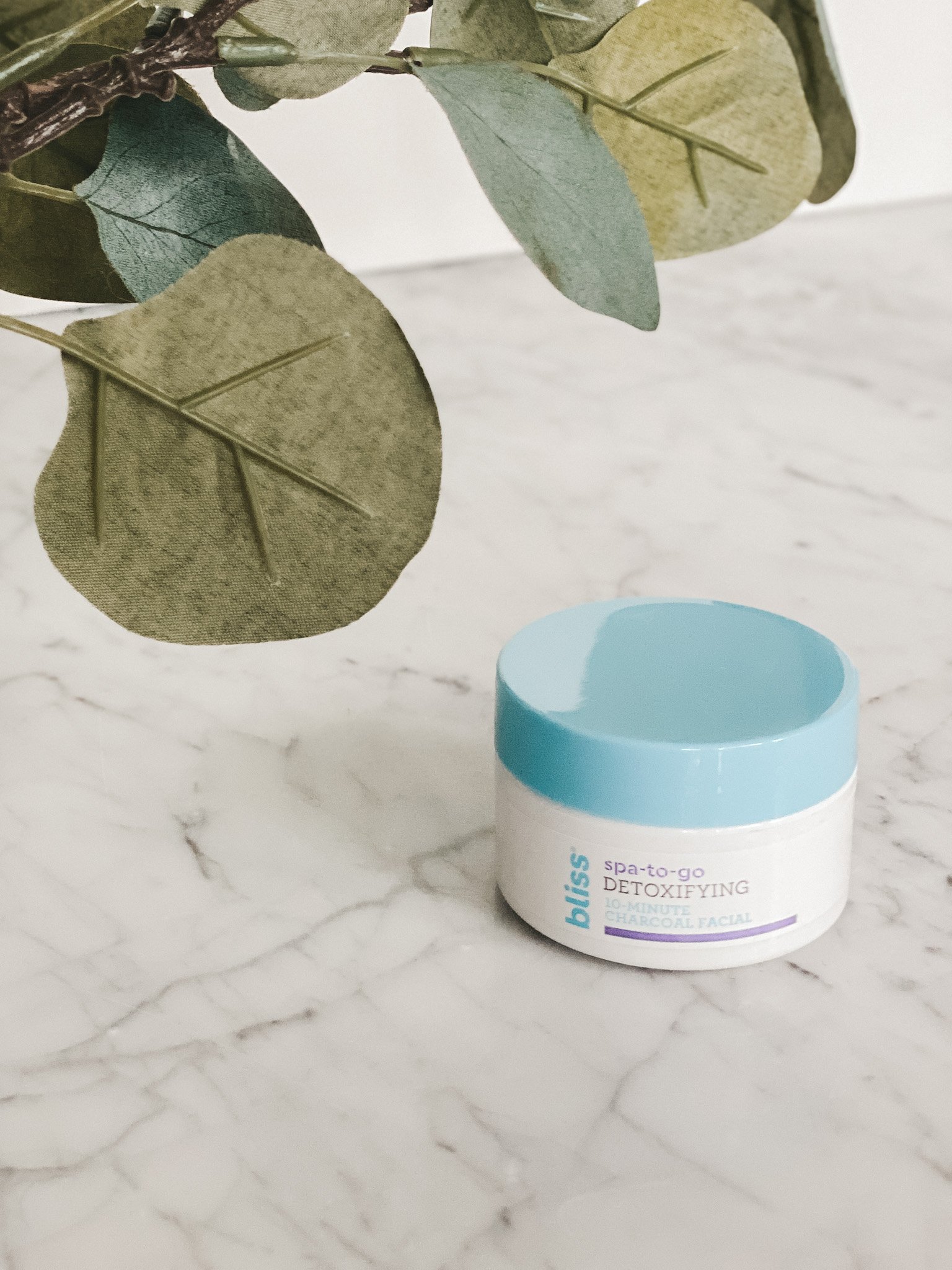 a marble table with a white jar with a blue lid set and eucalyptus leaves in the corner