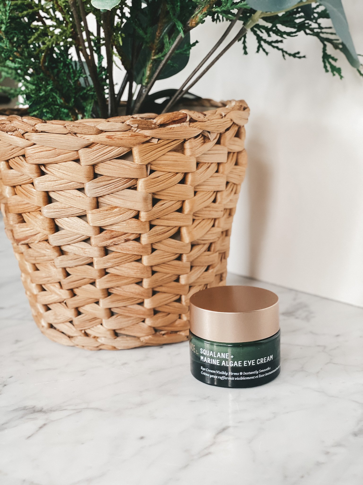 a marble table with a white background; a green jar with a gold lid and a woven basket with a potted plant