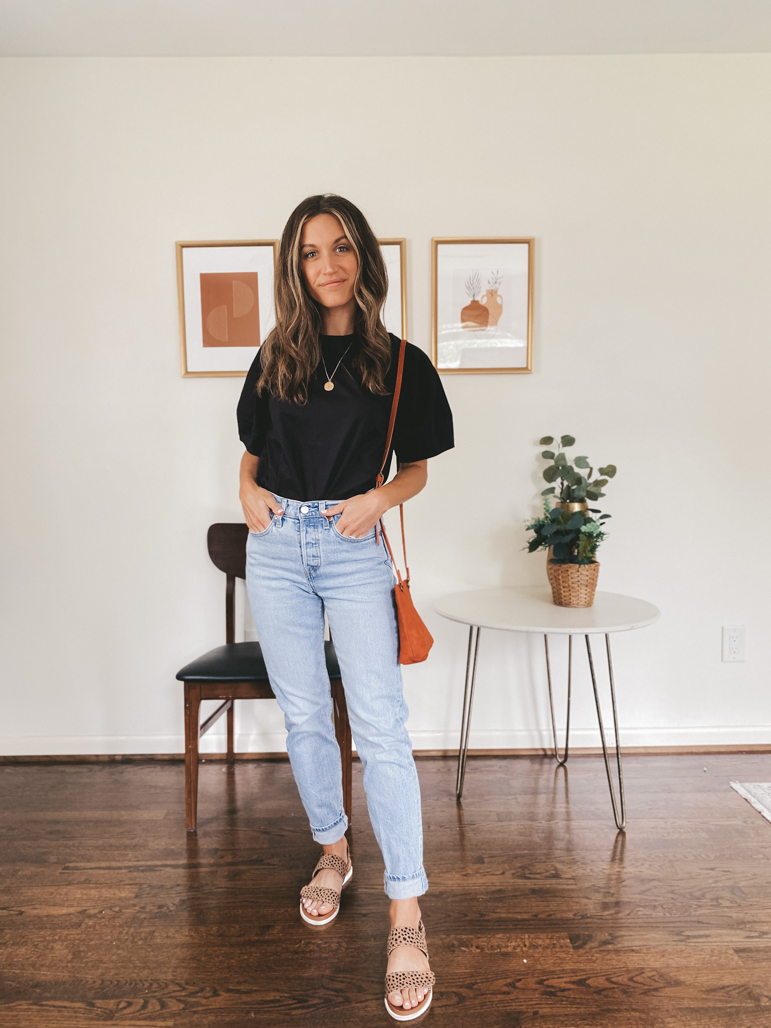 ashley wearing a black short sleeved top, light wash mom jeans and leopard print sandals with a red crossbody bag