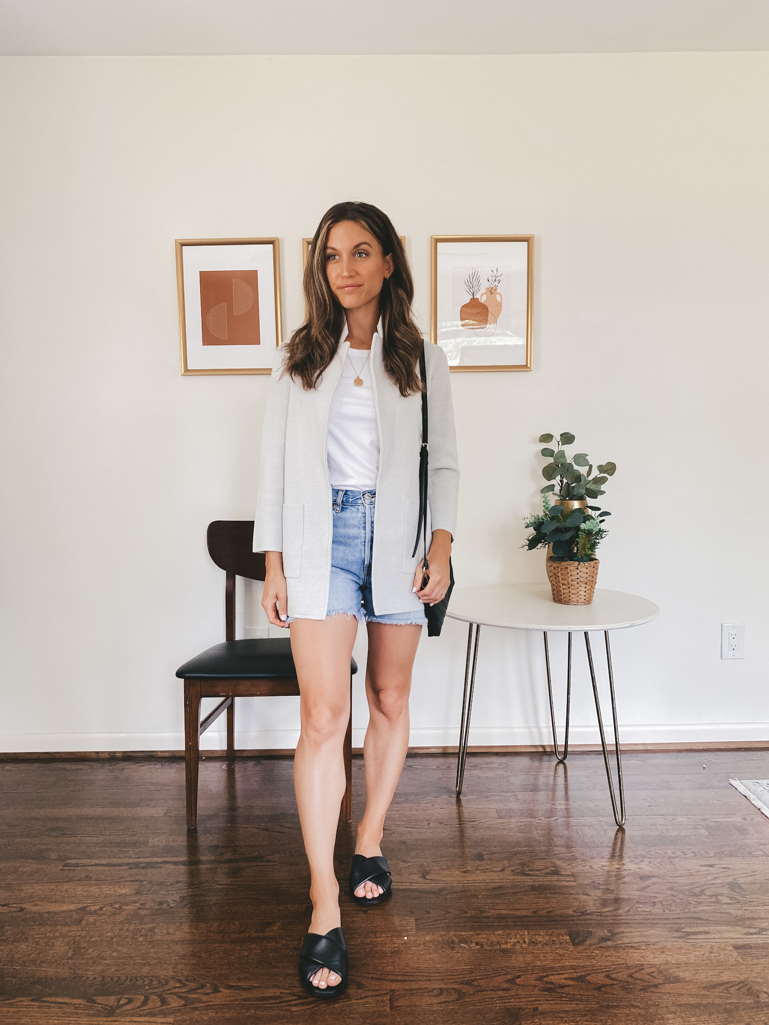 ashley wearing a white tank under a light gray sweater blazer, denim cut-off shorts and black crossover slides