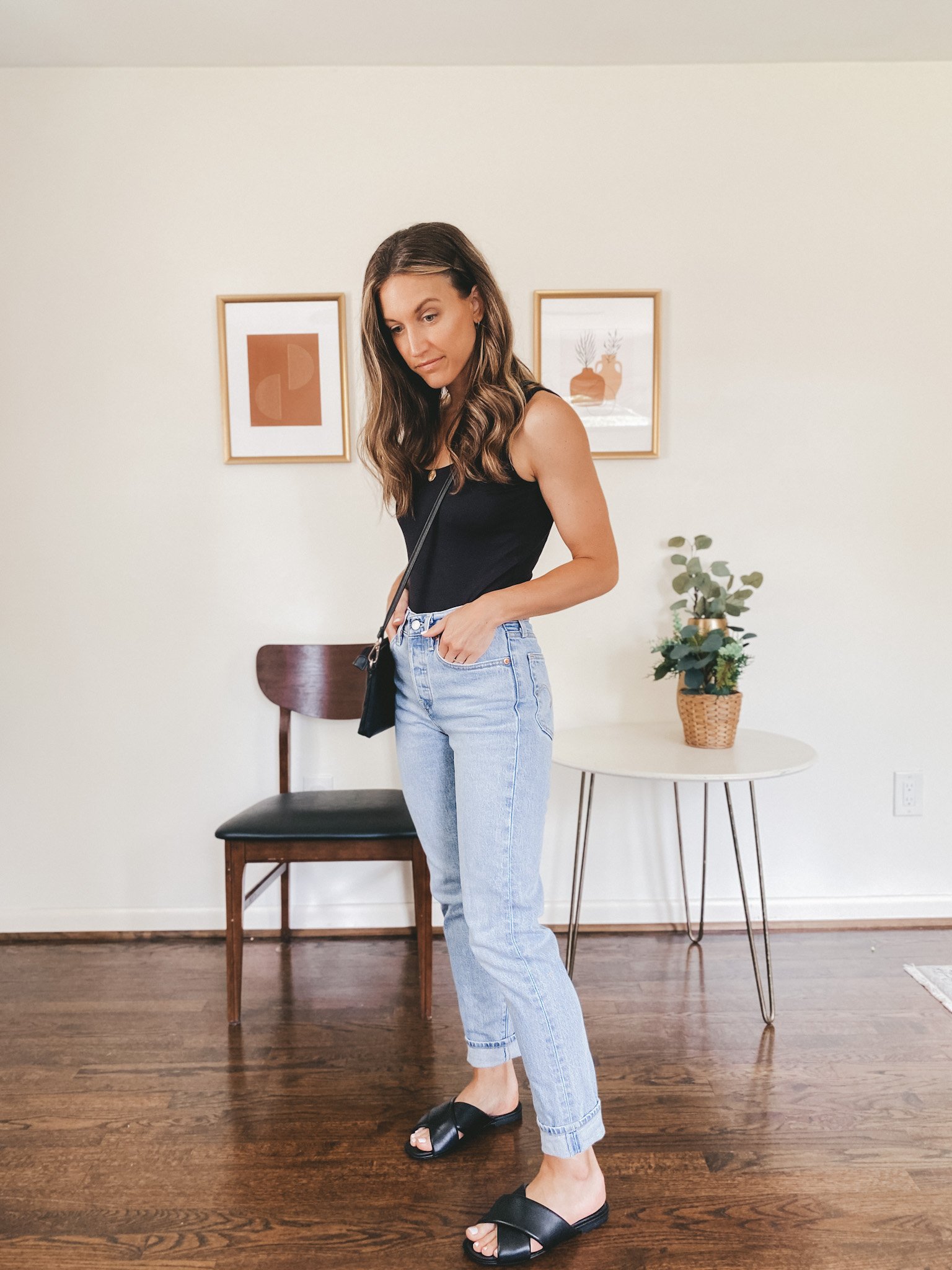 ashley wearing a black bodysuit, light wash mom jeans and black crossover slides