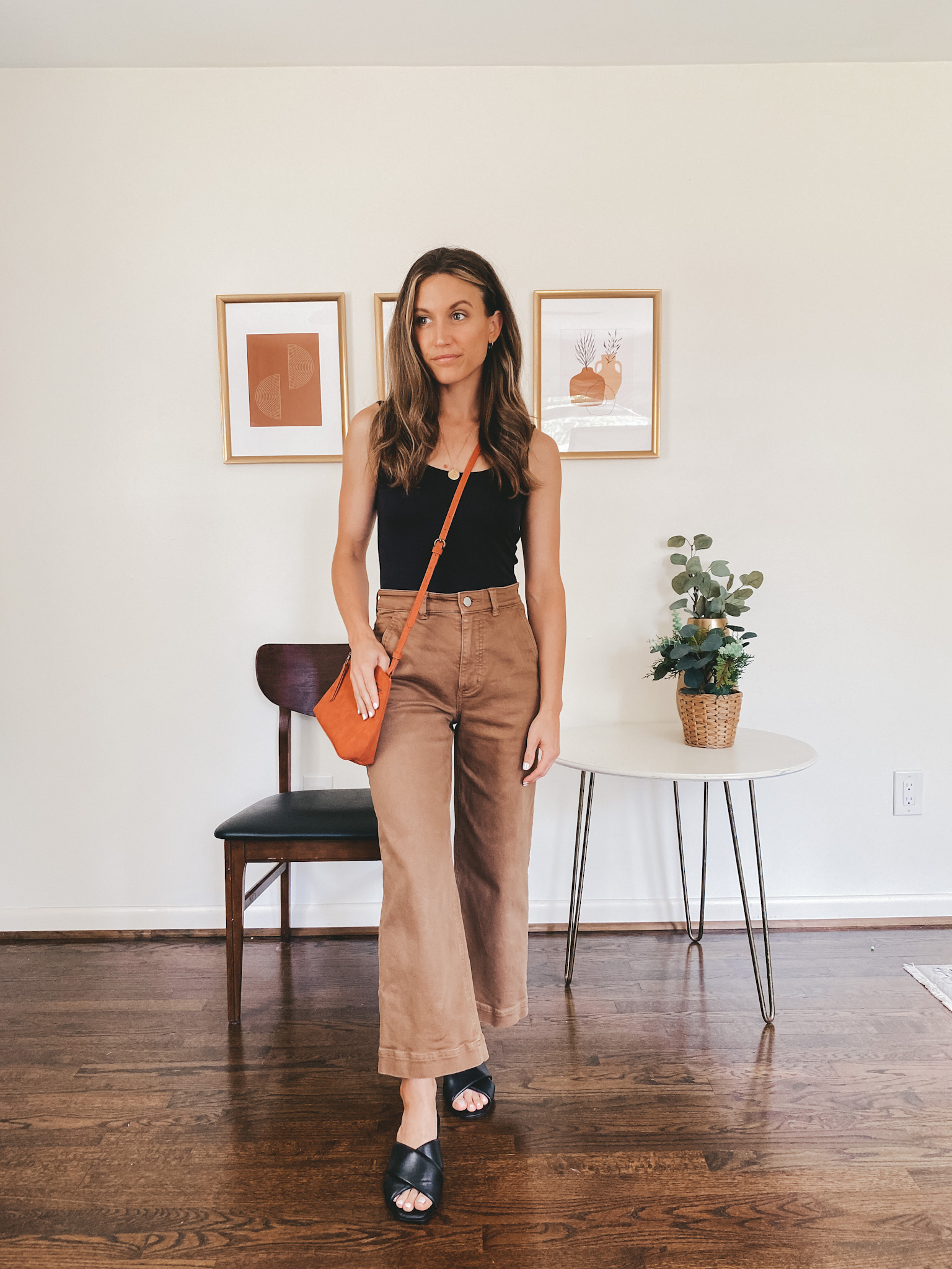 ashley wearing a black bodysuit, brown wide leg crop pants and black slides with a red crossbody bag