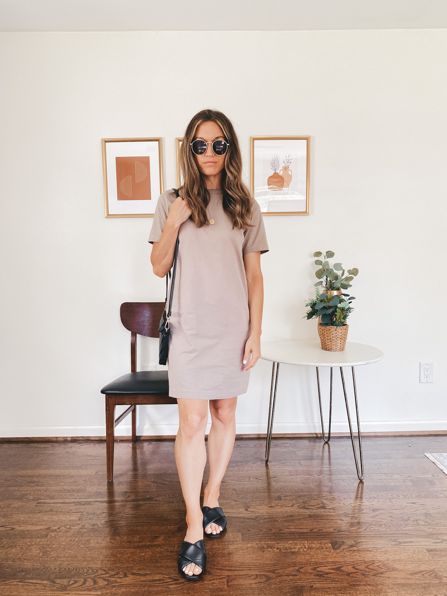 ashley wearing a taupe t-shirt dress, black crossover slides and round gold frame sunglasses