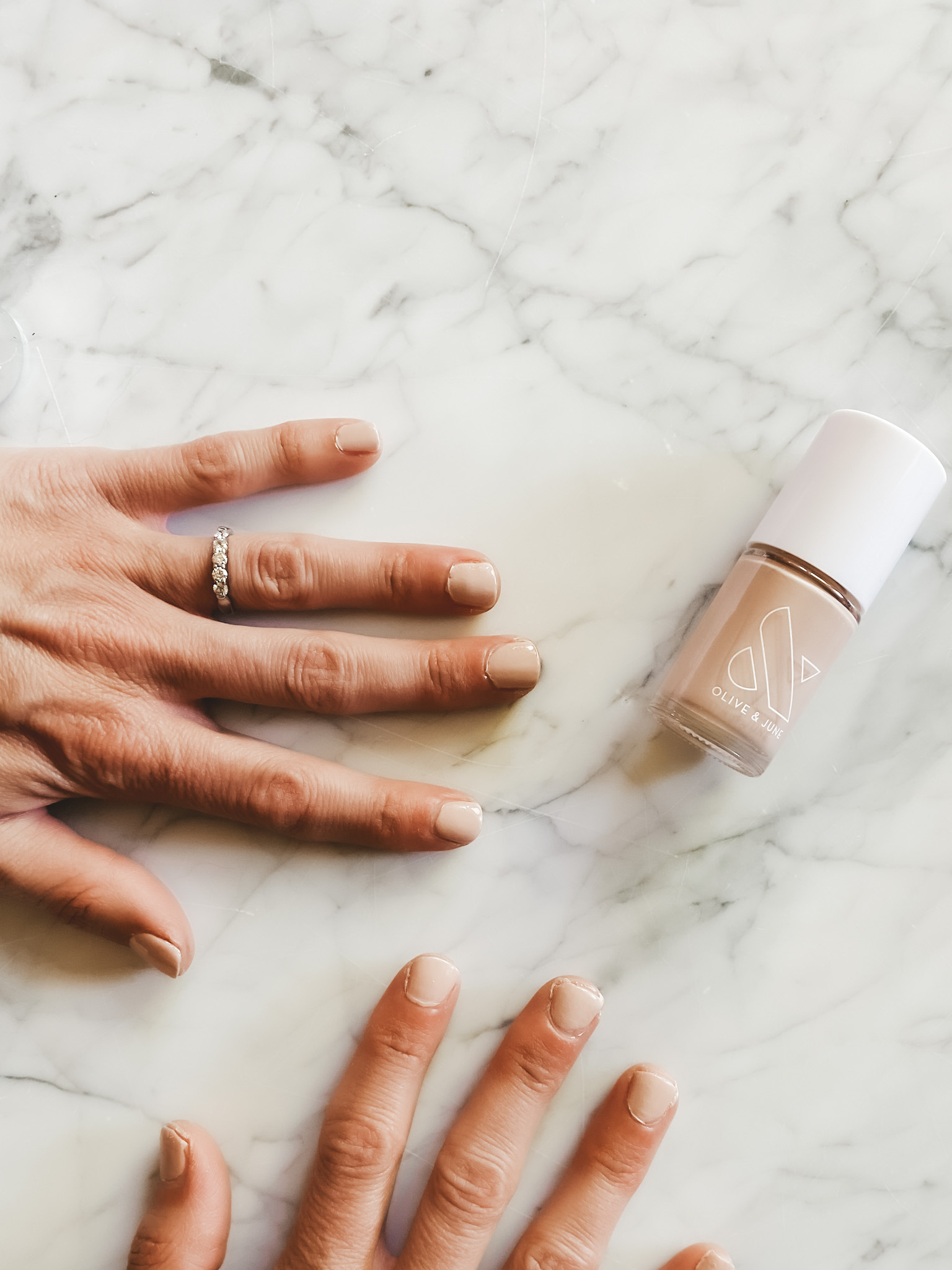 two hands with painted nails and a bottle of nail polish on a marble table