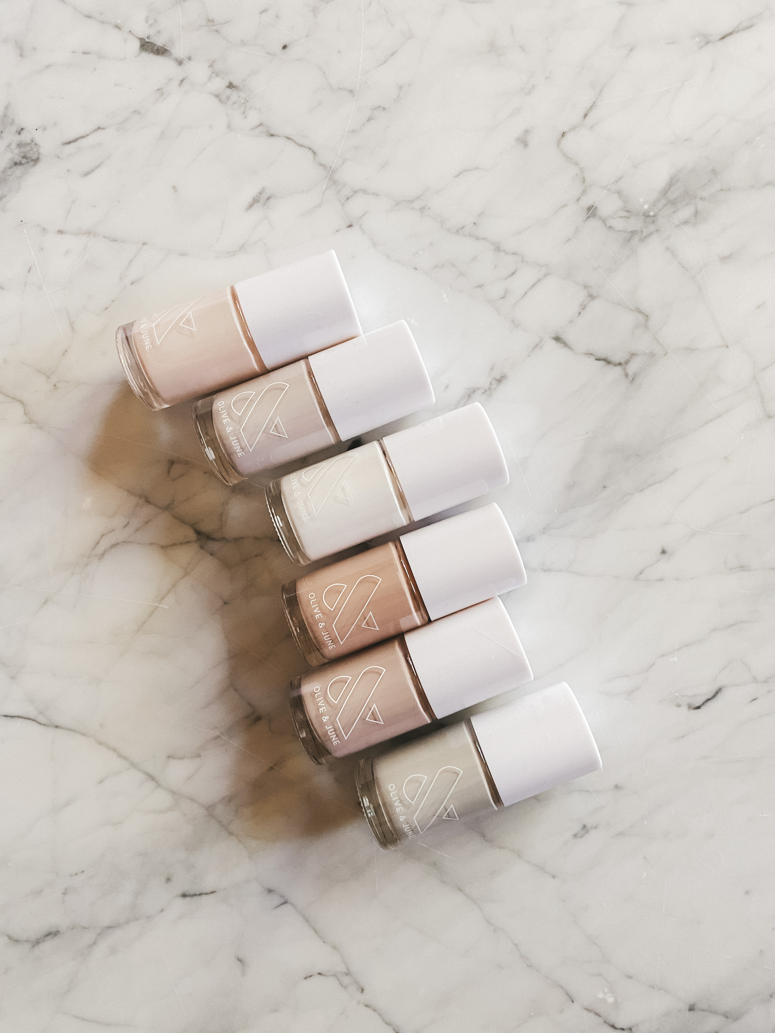 a set of six Olive and June nail polishes in different shades on a marble table