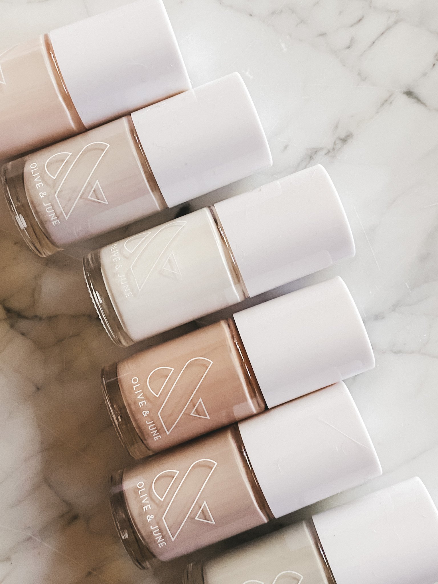 a set of six Olive and June nail polishes in different shades on a marble table