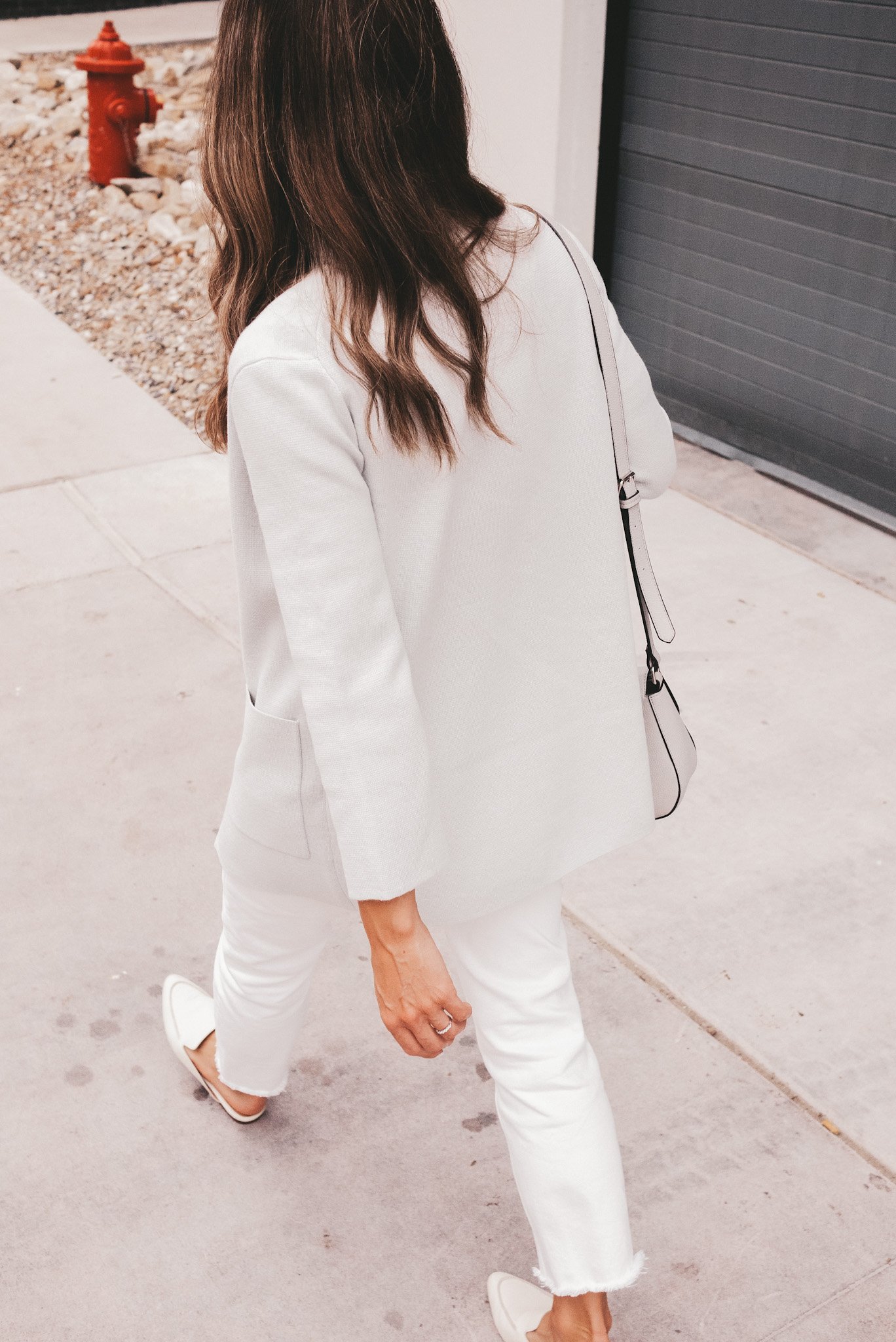 ashley walking down a sidewalk wearing a gray sweater blazer, white jeans and white mules