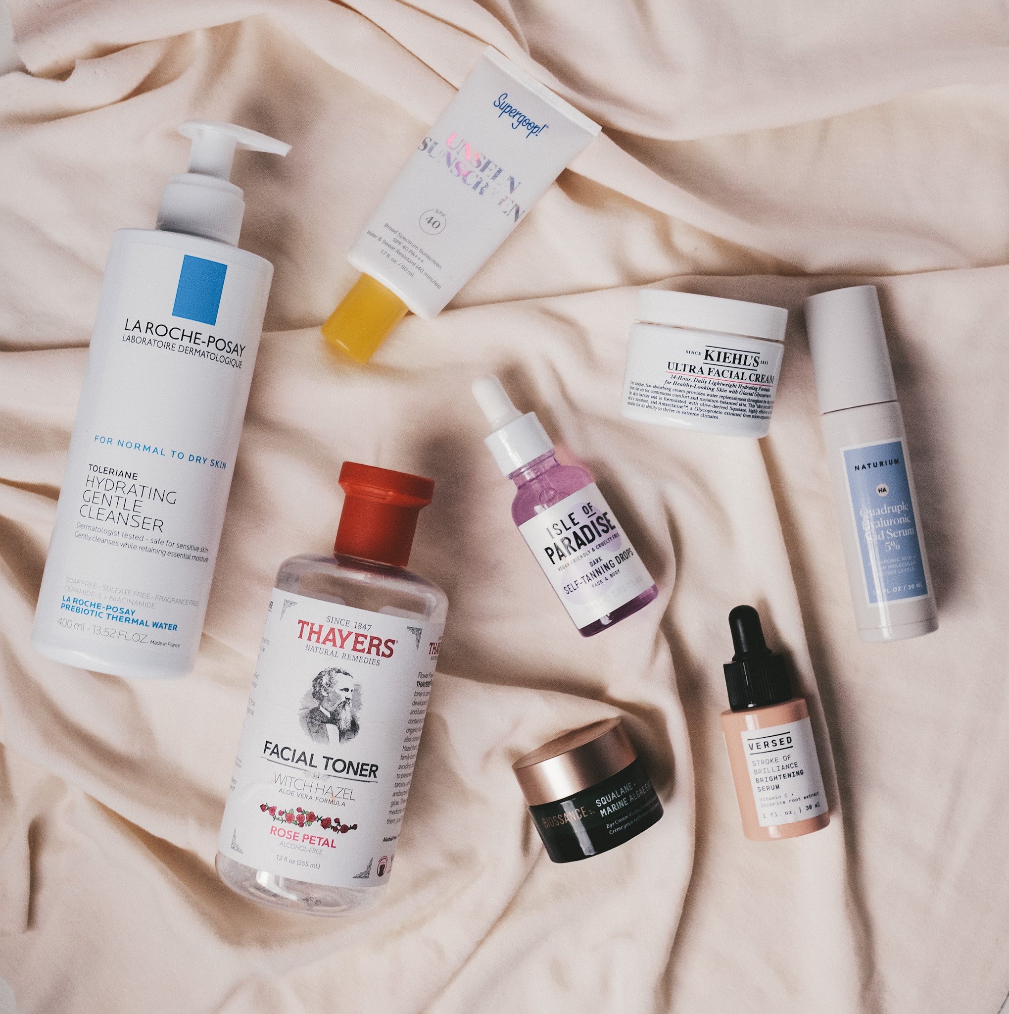 a overhead shot with a cream colored fabric and various skincare products on top that are used in the morning as part of my summer skincare routine