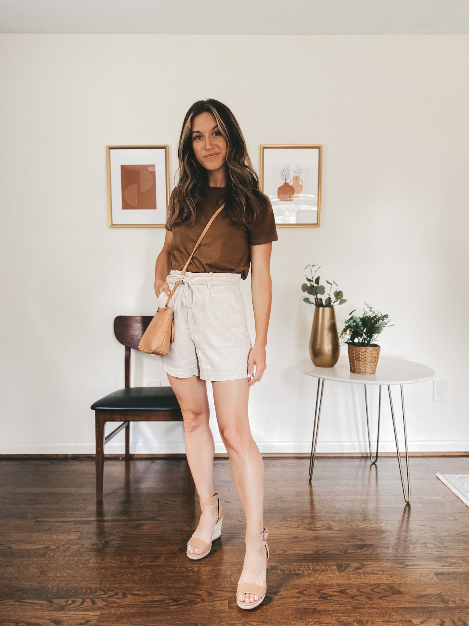 ashley wearing a walnut colored tee, tan linen shorts, and tan espadrilles with a camel colored crossbody bag