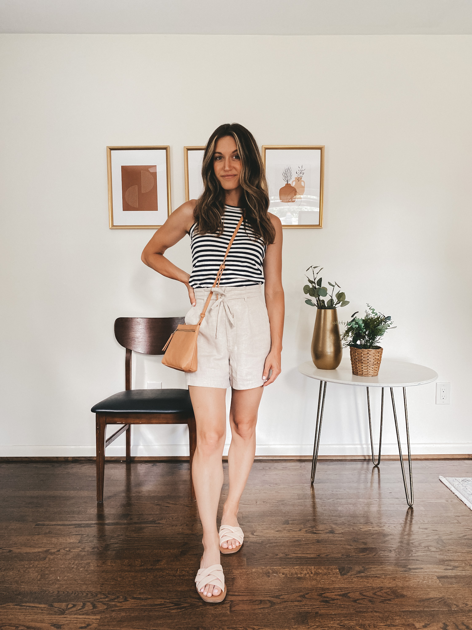 ashley wearing a navy and white striped tank, tan linen shorts and nude padded slides with a camel colored crossbody bag