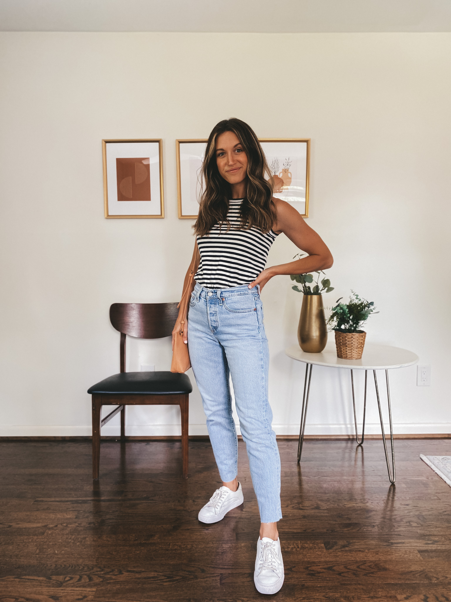 ashley wearing a navy and white striped tank, light wash straight leg denim and white sneakers with a camel colored crossbody bag