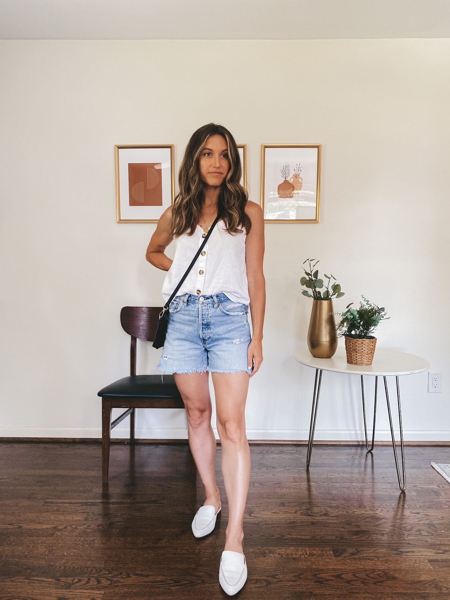 ashley wearing a white button front linen tank, cut-off denim shorts and white mules