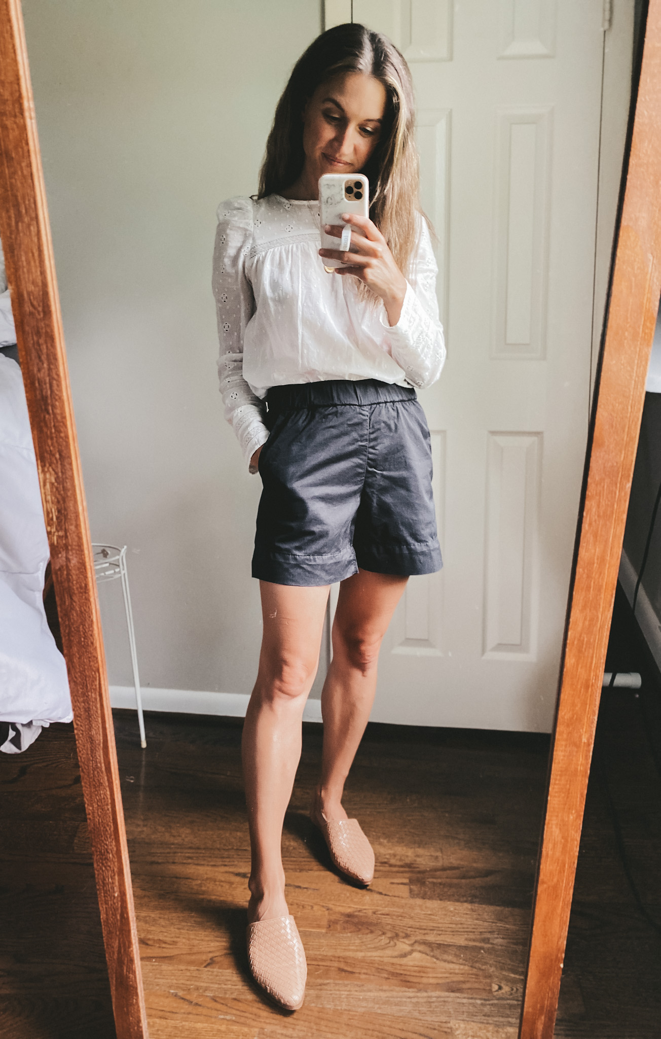 ashley wearing a long sleeved eyelet top, black chino shorts, and tan woven mules