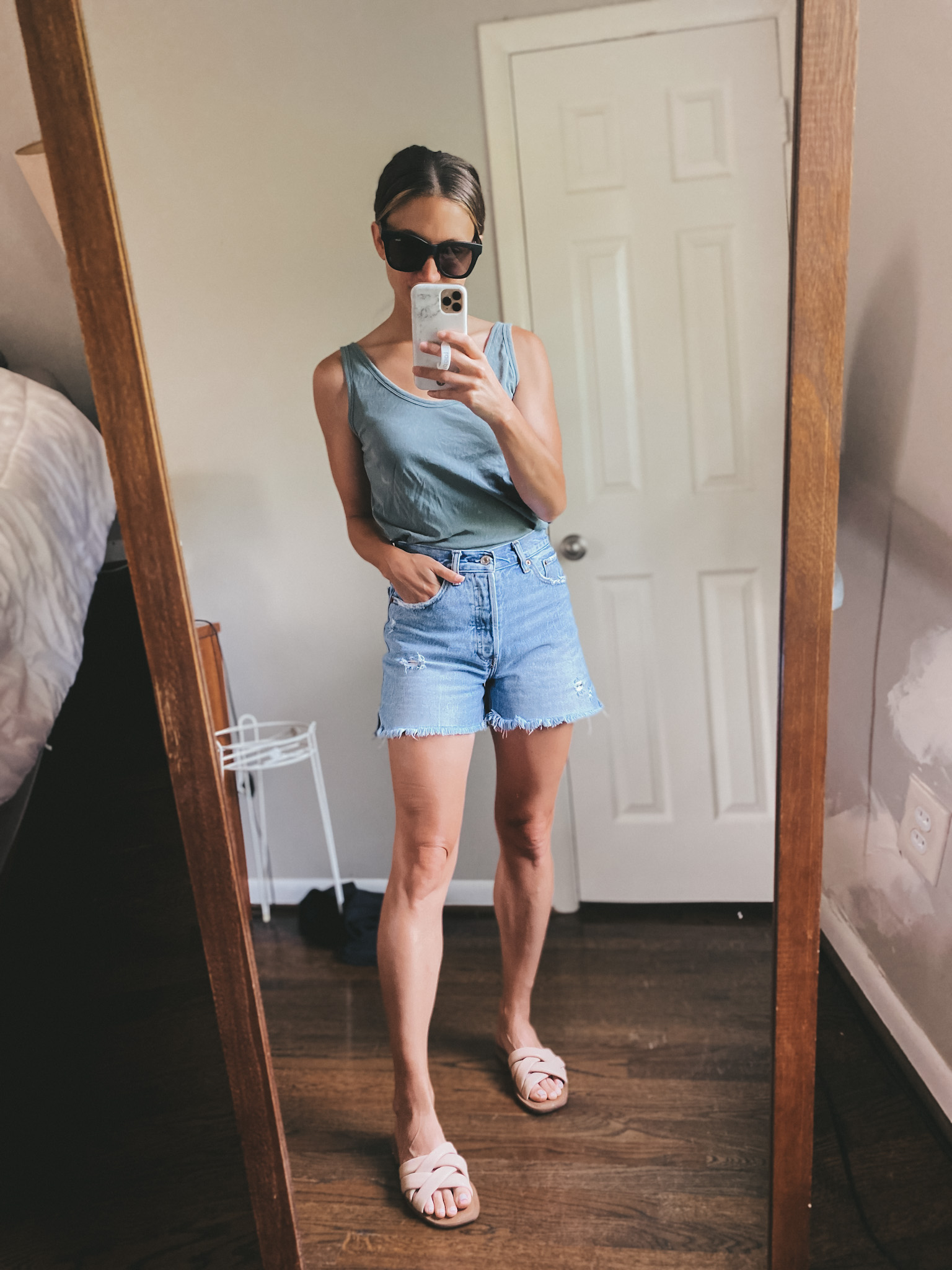 ashley wearing a light blue tank, cut-off denim shorts and nude padded slides