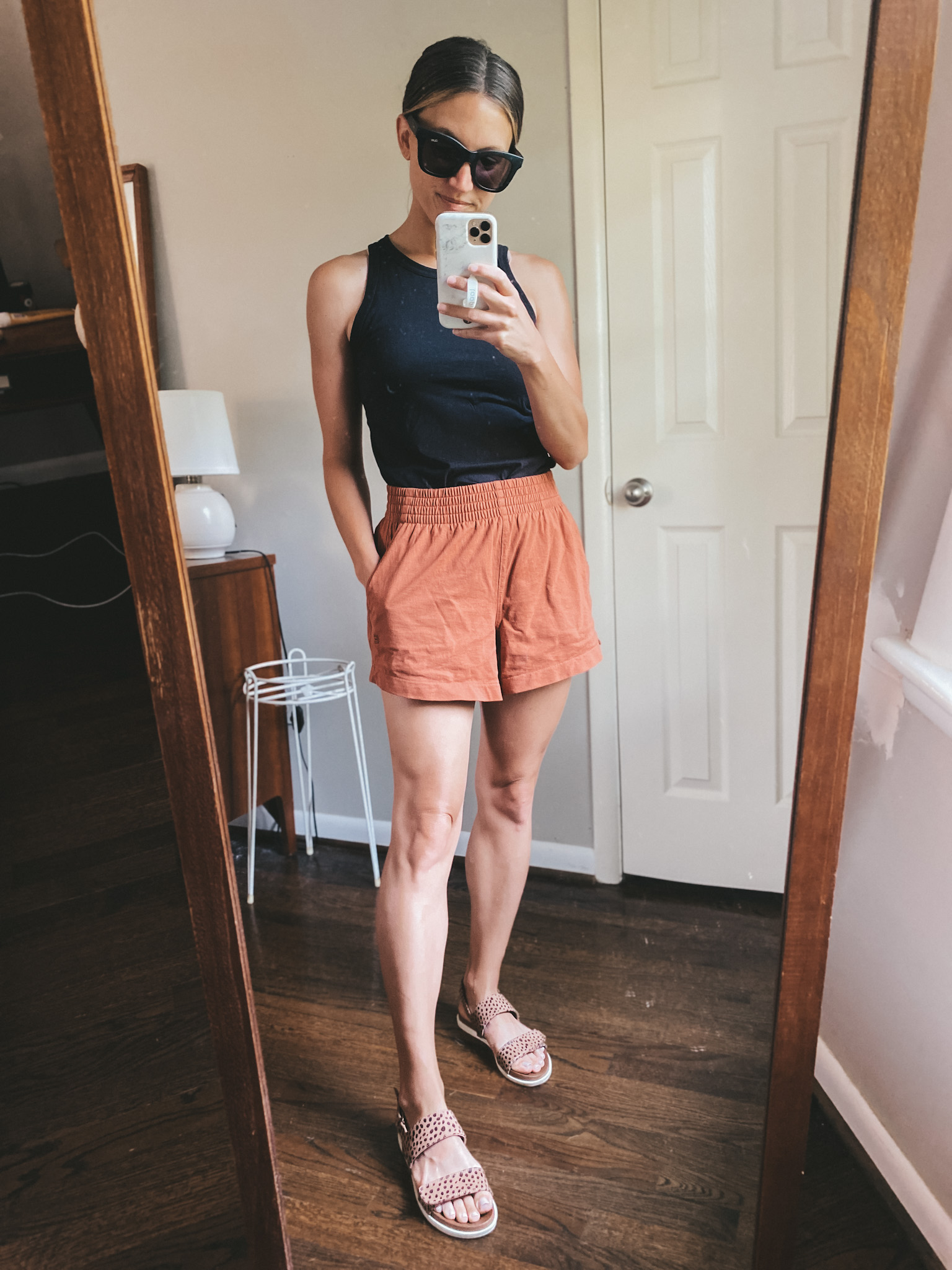 ashley wearing a black tank, rust colored jersey shorts and leopard print sandals with square frame black sunglasses