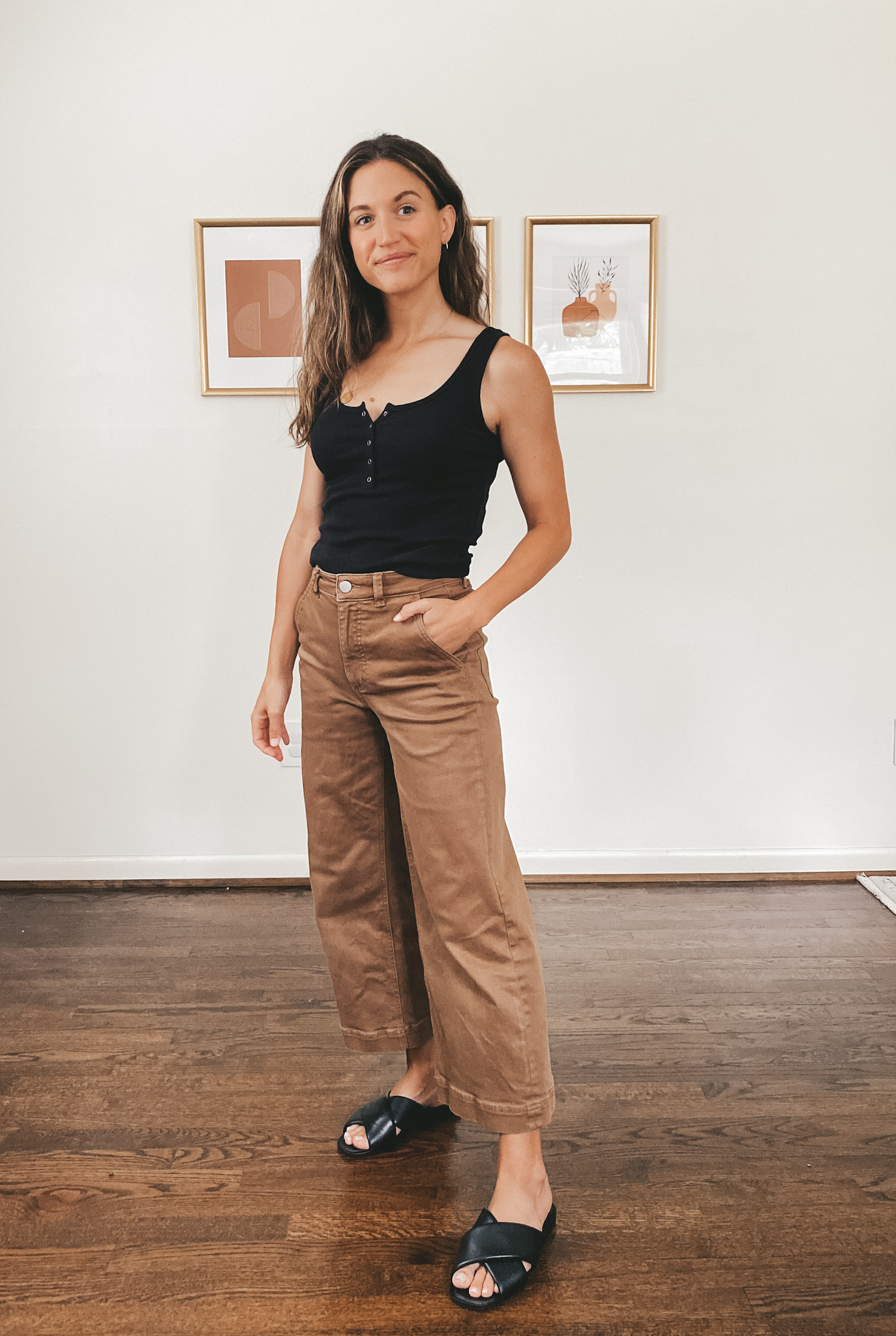 ashley wearing a black henley tank, brown wide leg cropped pants, and black crossover slides