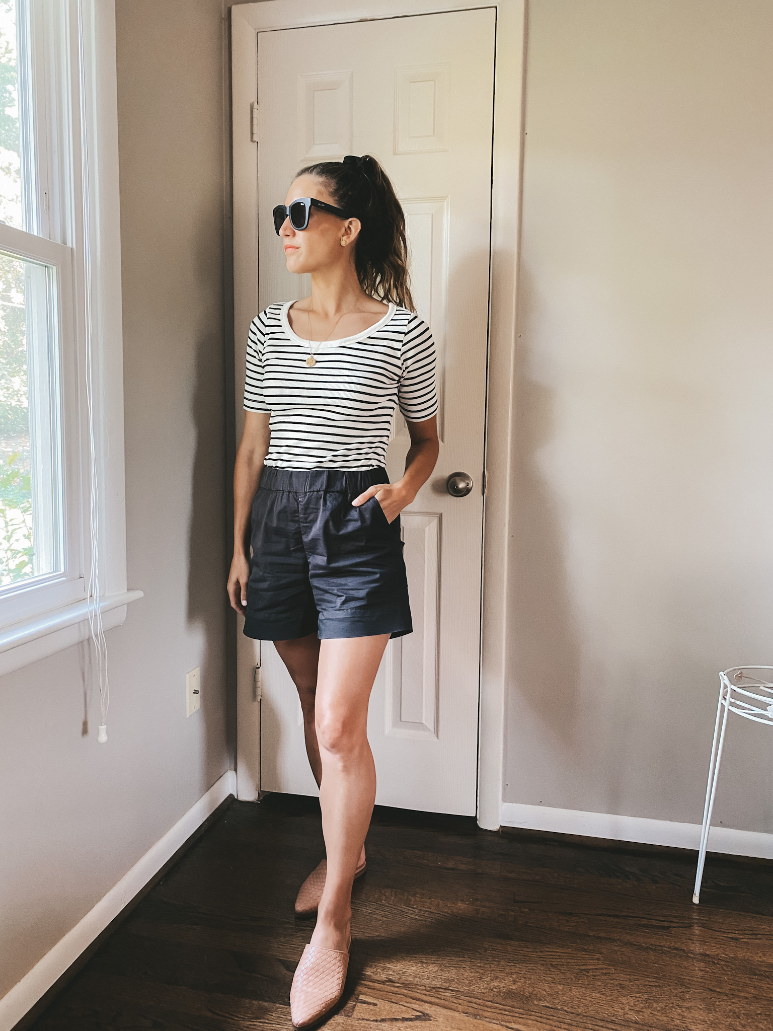 ashley wearing a black and white striped tee, black chino shorts, and tan woven mules with black square frame sunglasses