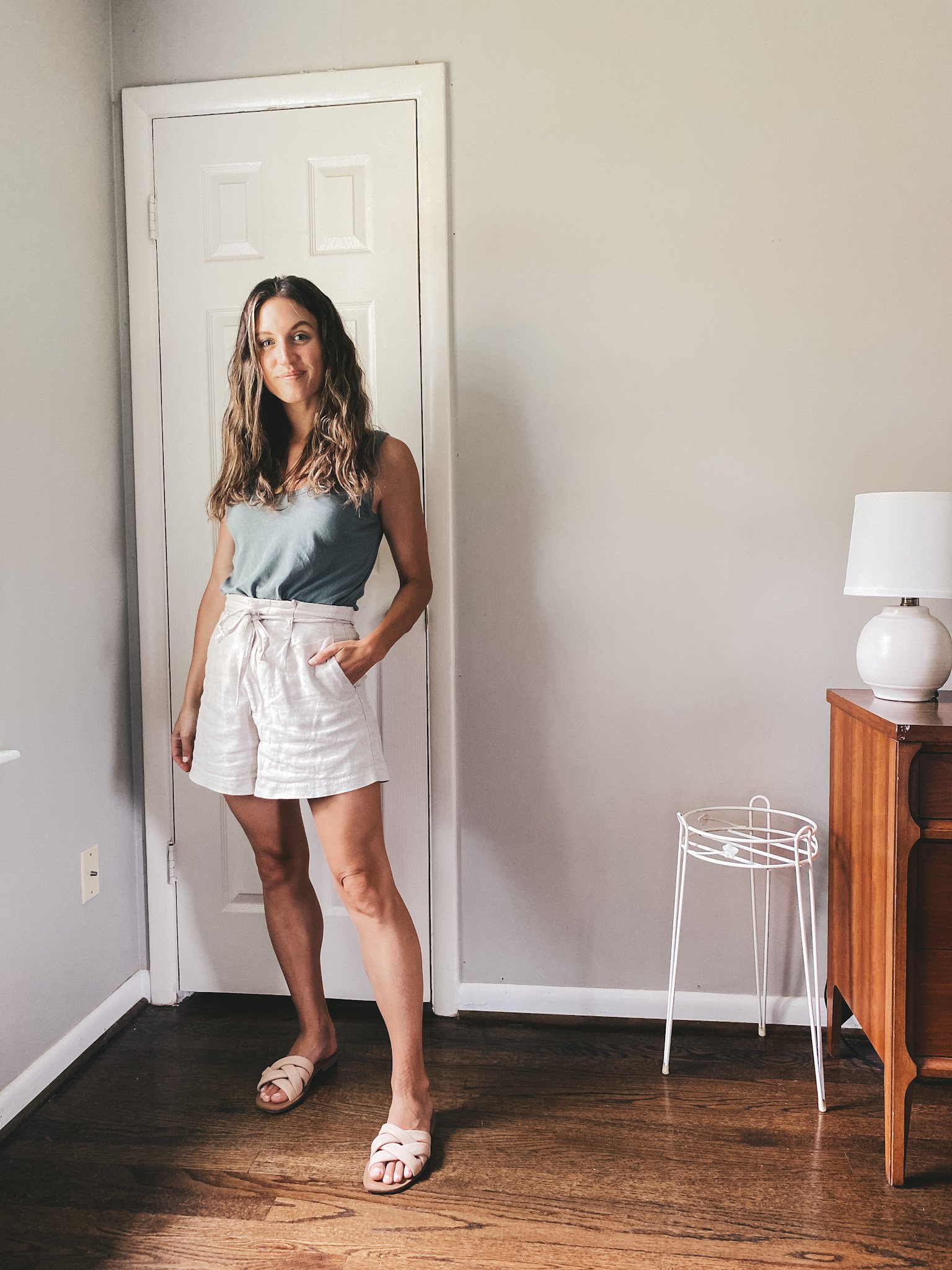 ashley wearing a blue tank, linen shorts, and nude padded slides