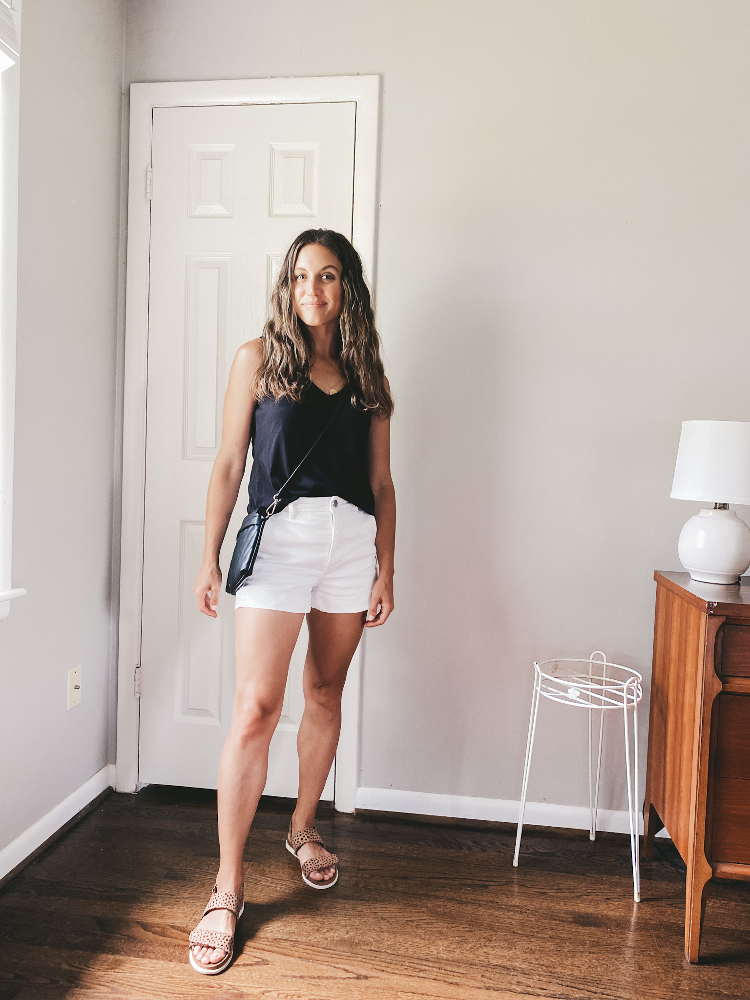 ashley wearing a black tank, white shorts, and leopard print sandals with a black crossbody bag