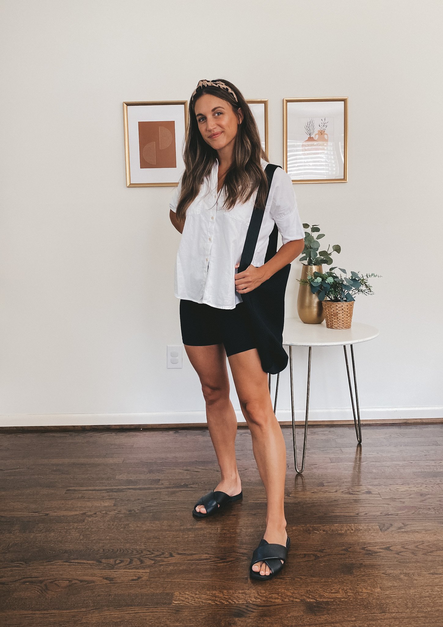 ashley wearing a white button down top, black biker shorts, black crossover slide sandals, a black tote bag and leopard print headband