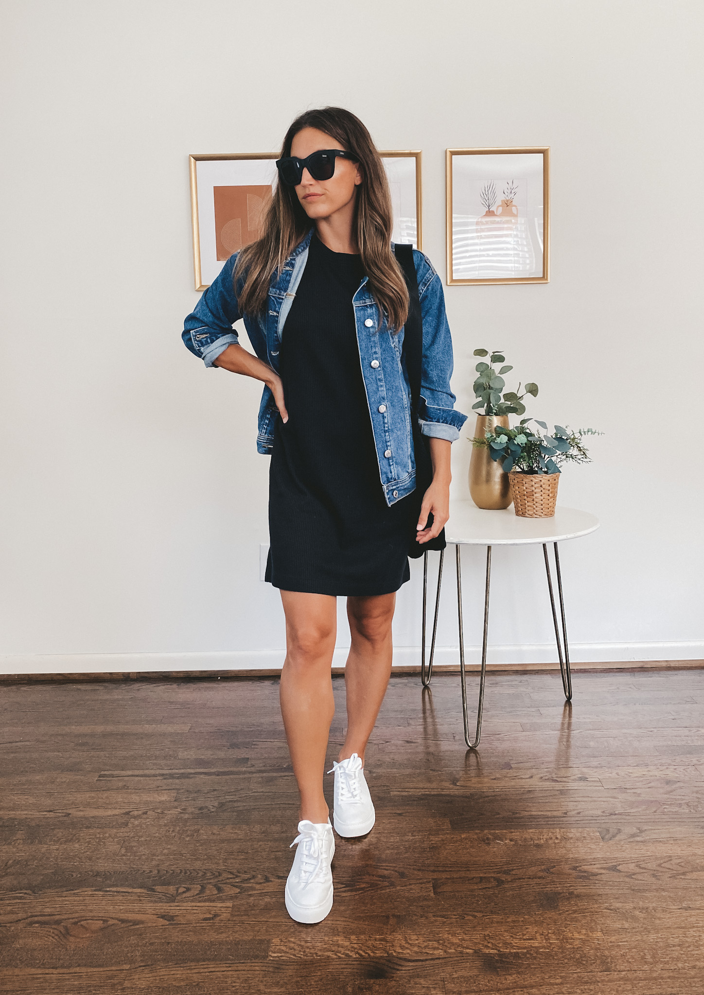 ashley wearing a black t-shirt dress, denim jacket, white sneakers, black square frame sunglasses, and a black tote bag