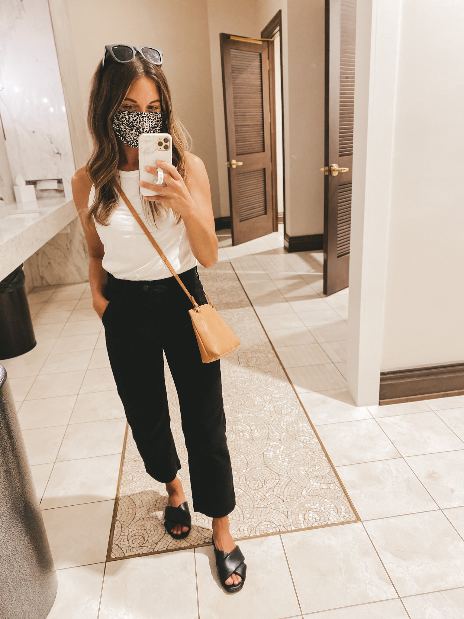 ashley wearing a white tank, black cropped pants, black crossover slide sandals, a brown purse, and a leopard print mask