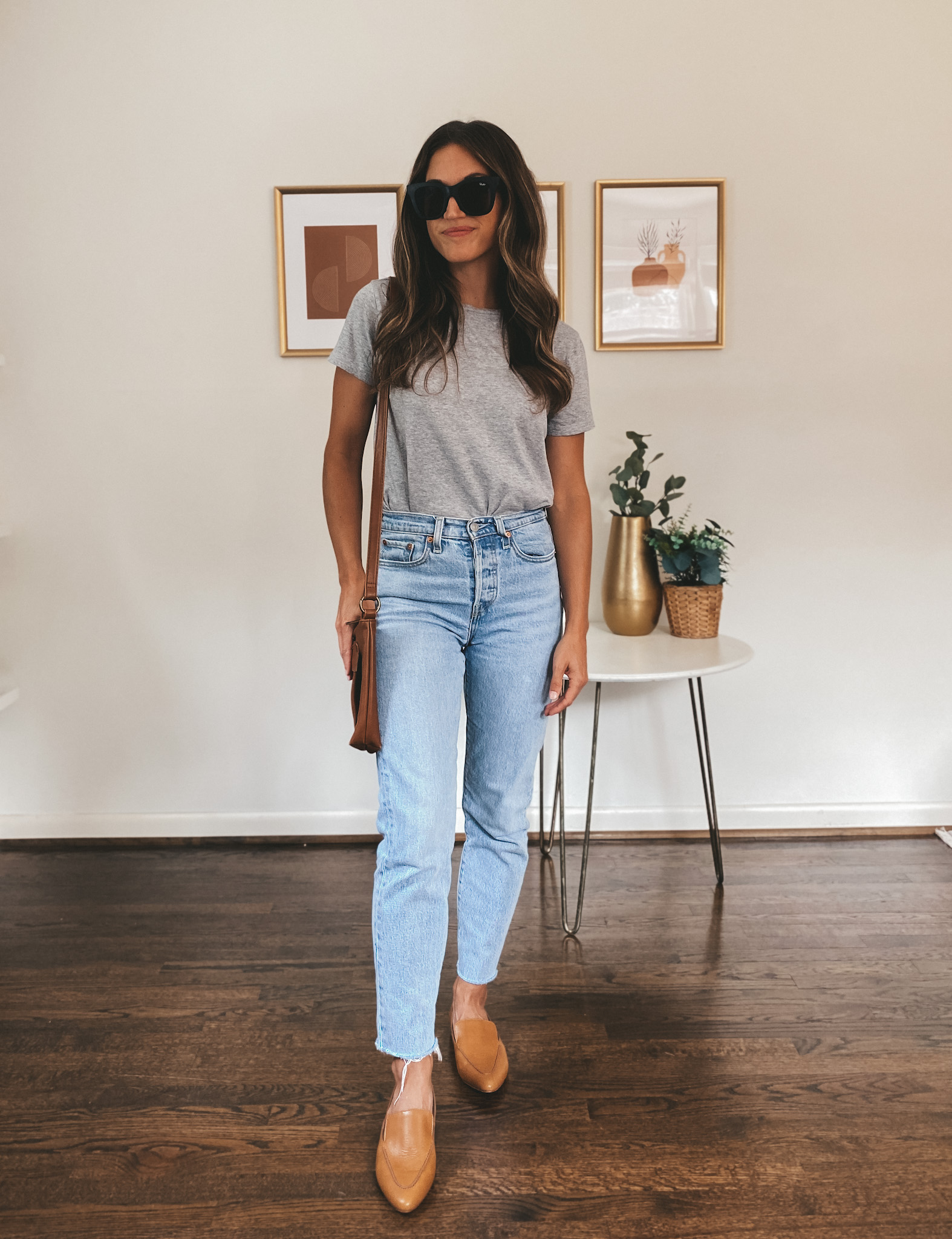 ashley wearing a gray tee, light wash mom jeans, cognac loafers, a cognac shoulder bag, and black square frame sunglasses