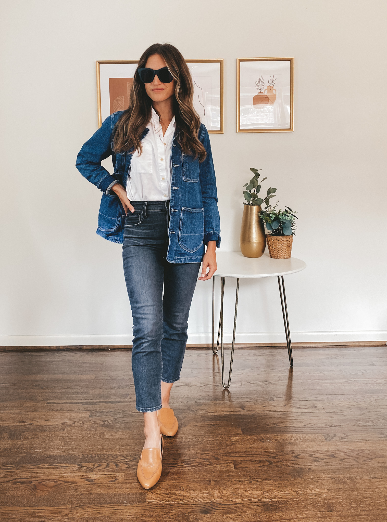 ashley wearing a white button down, washed black denim, a denim chore jacket and cognac loafers with black square frame sunglasses