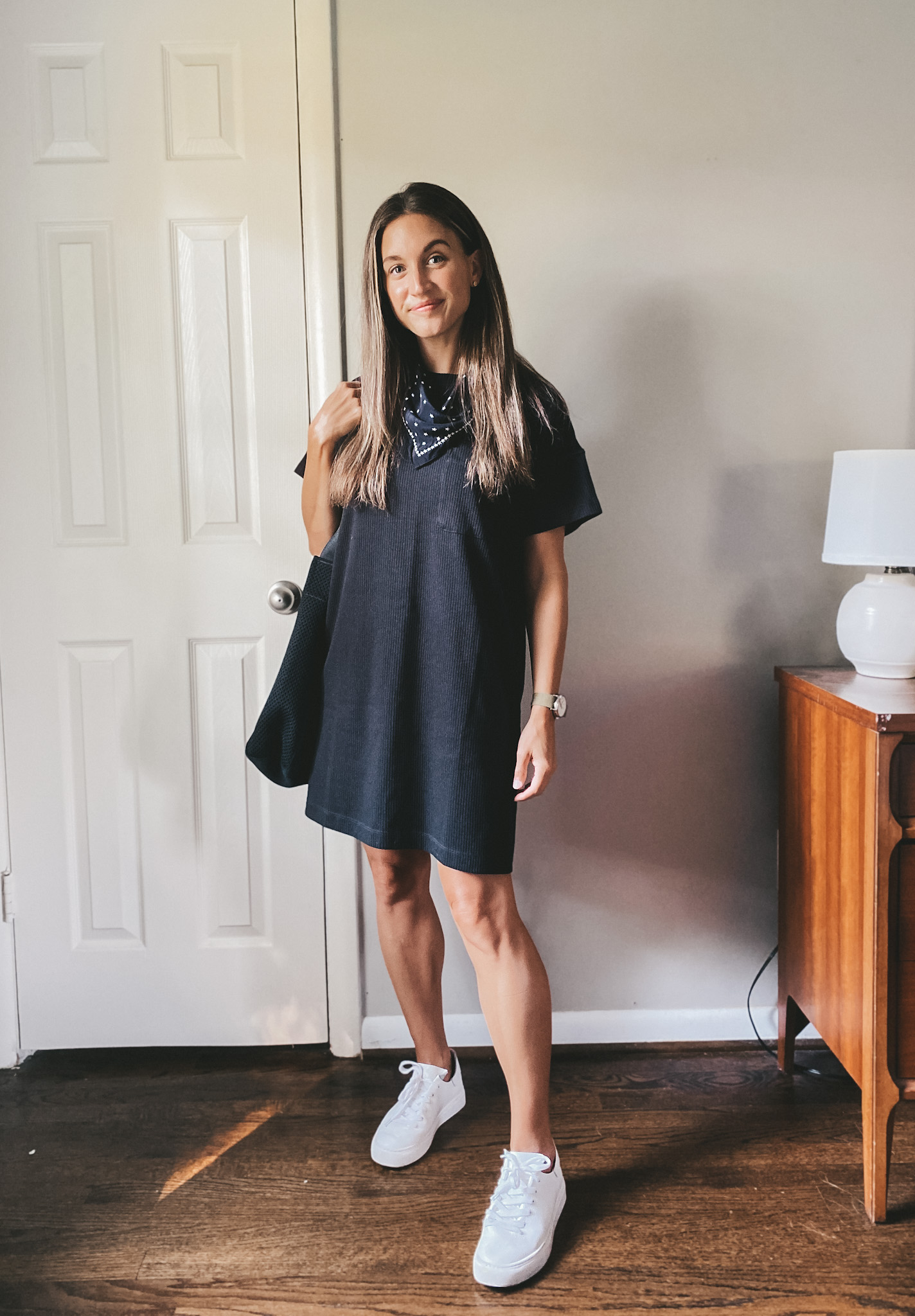 ashley wearing a black t-shirt dress, white sneakers, and black and white patterned bandana tied around the neck and a black tote bag