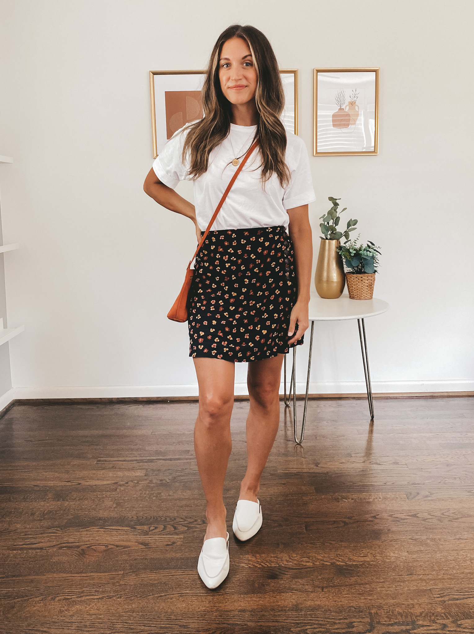 ashley wearing a white tee, black floral mini skirt, white mules, and an orange crossbody purse