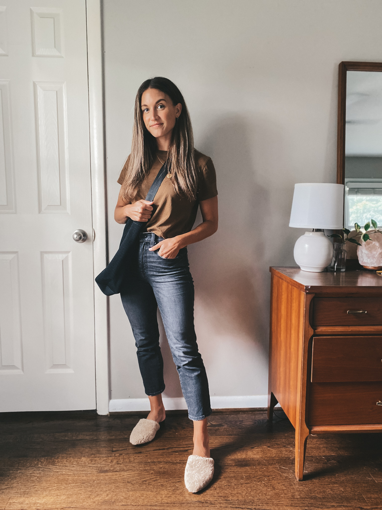 ashley wearing a brown tee, washed black jeans, tan shearling mules, and a black tote bag