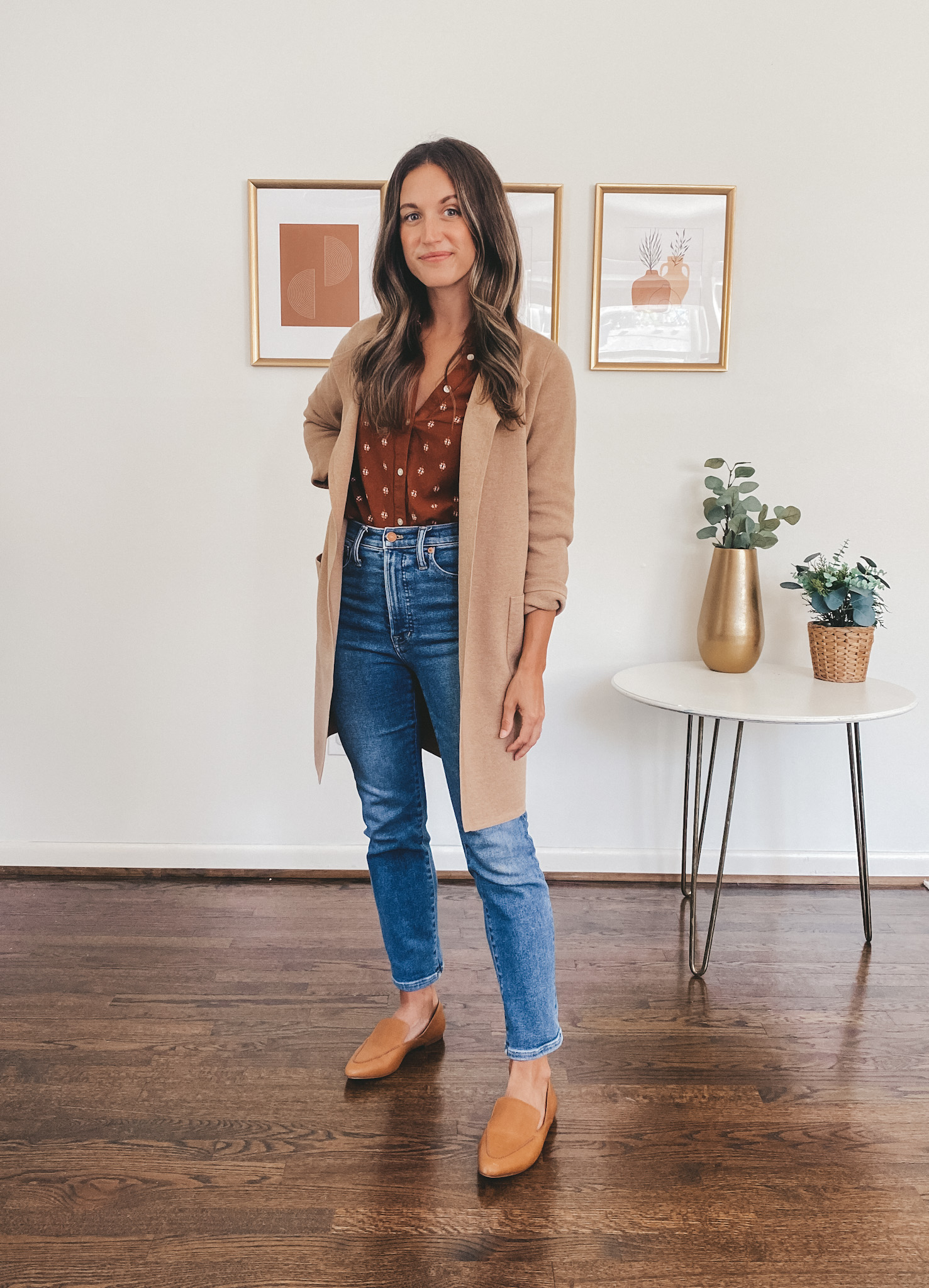 ashley wearing a dark orange patterned peasant blouse under a tan coatigan sweater blazer, medium wash jeans, and cognac loafers